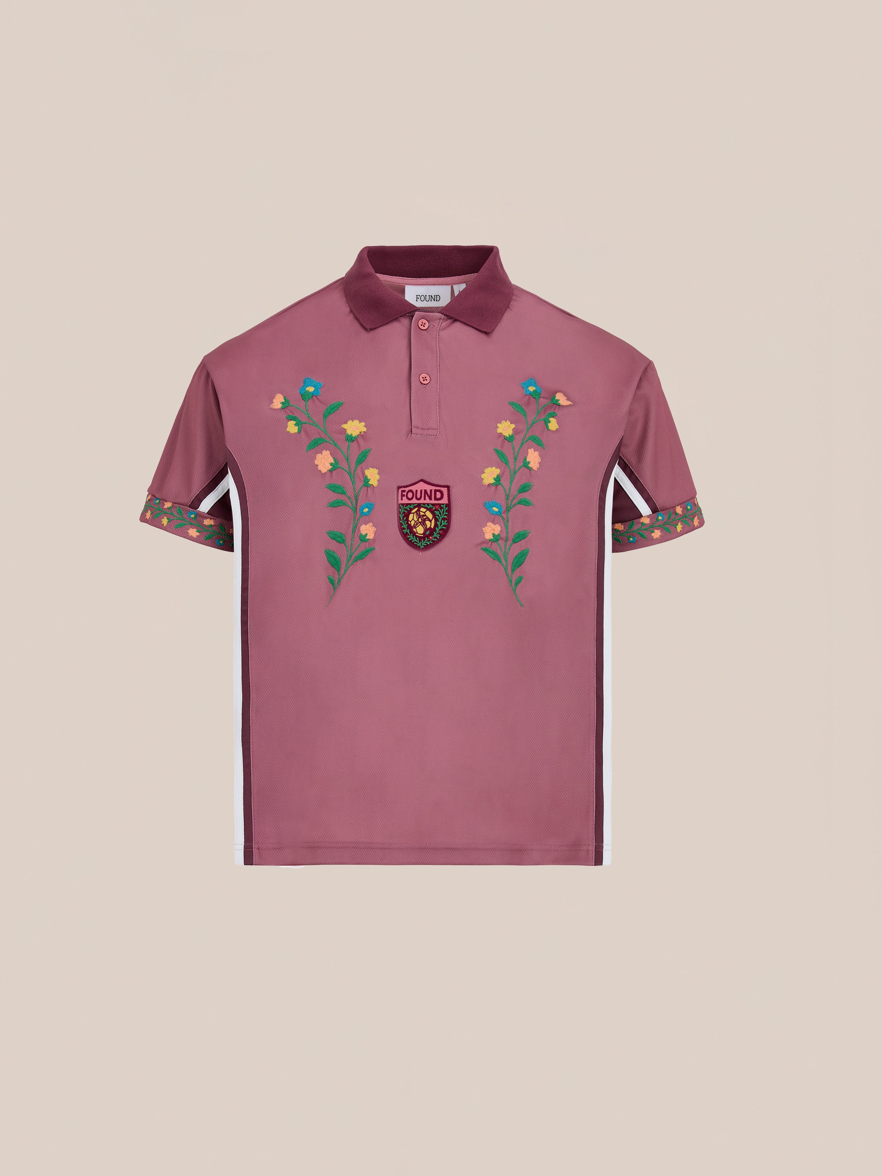 The FOUND Floral Polo Jersey is a mauve cotton polo with floral embroidery on the chest and sleeves, plus a small "FOUND" crest patch, inspired by vintage football shirts.