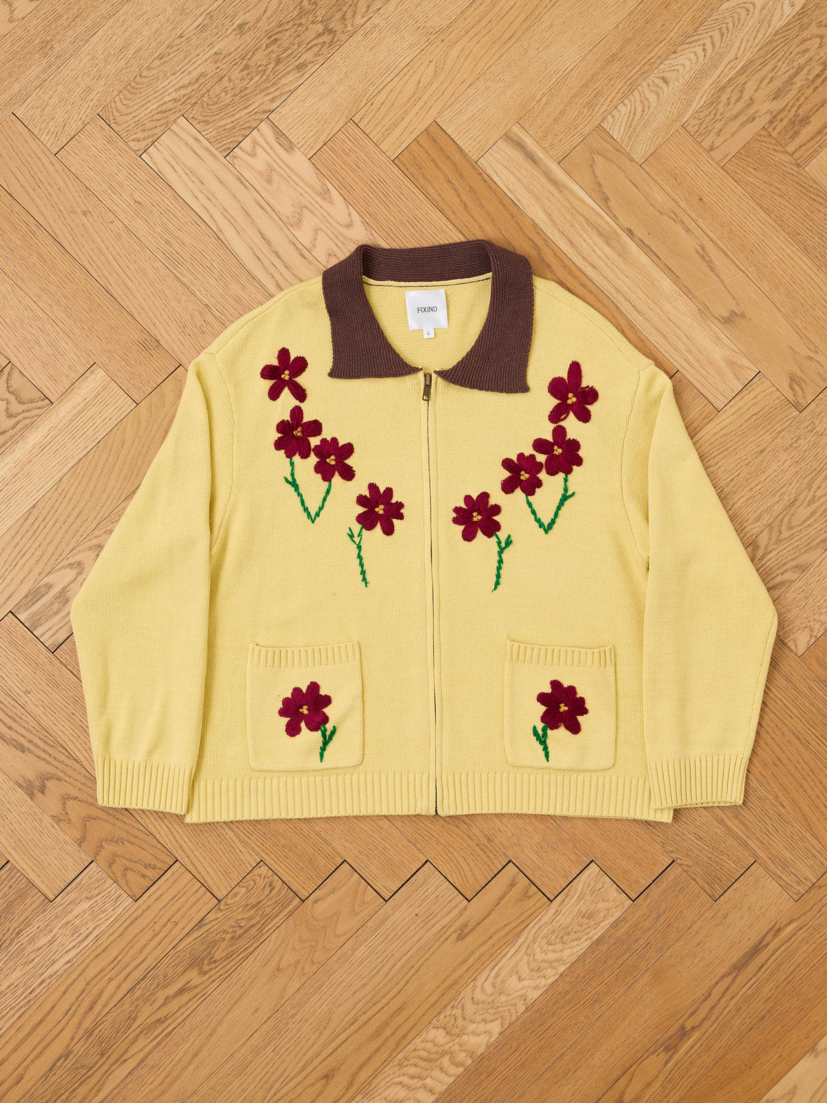 The Floral Sun Knit Sweater by FOUND features yellow knits, a brown collar, red flower appliqués, and green embroidered stems for vintage-inspired charm.