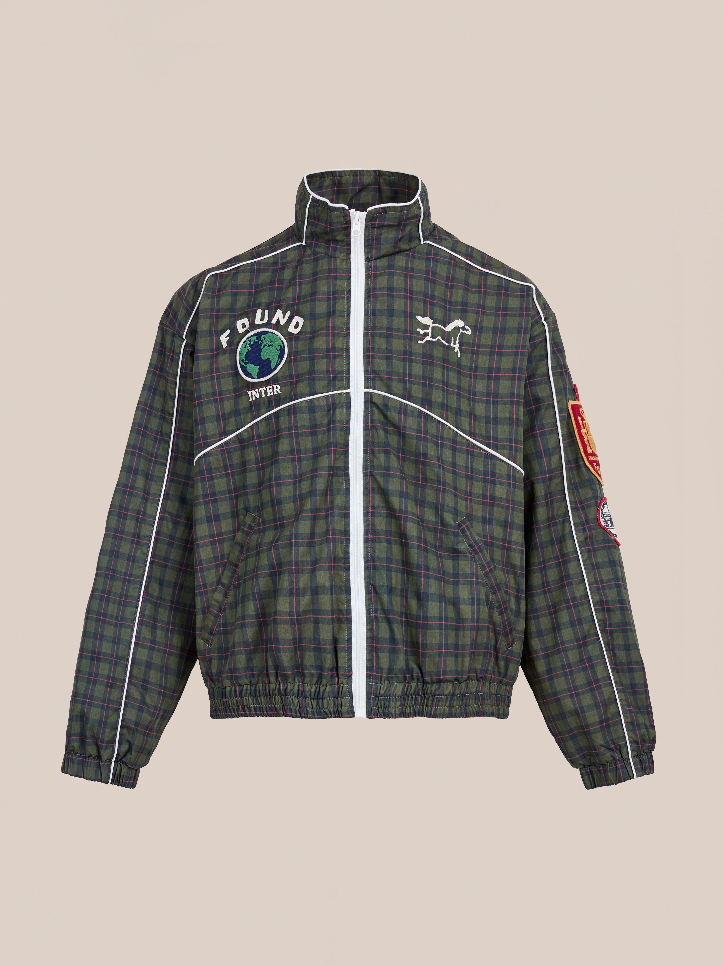The FOUND Forest Plaid Track Jacket is a lightweight cotton zip-up featuring white piping, embroidered patches—a horse, globe, "FOUND" on the chest—and a red patch on the sleeve.