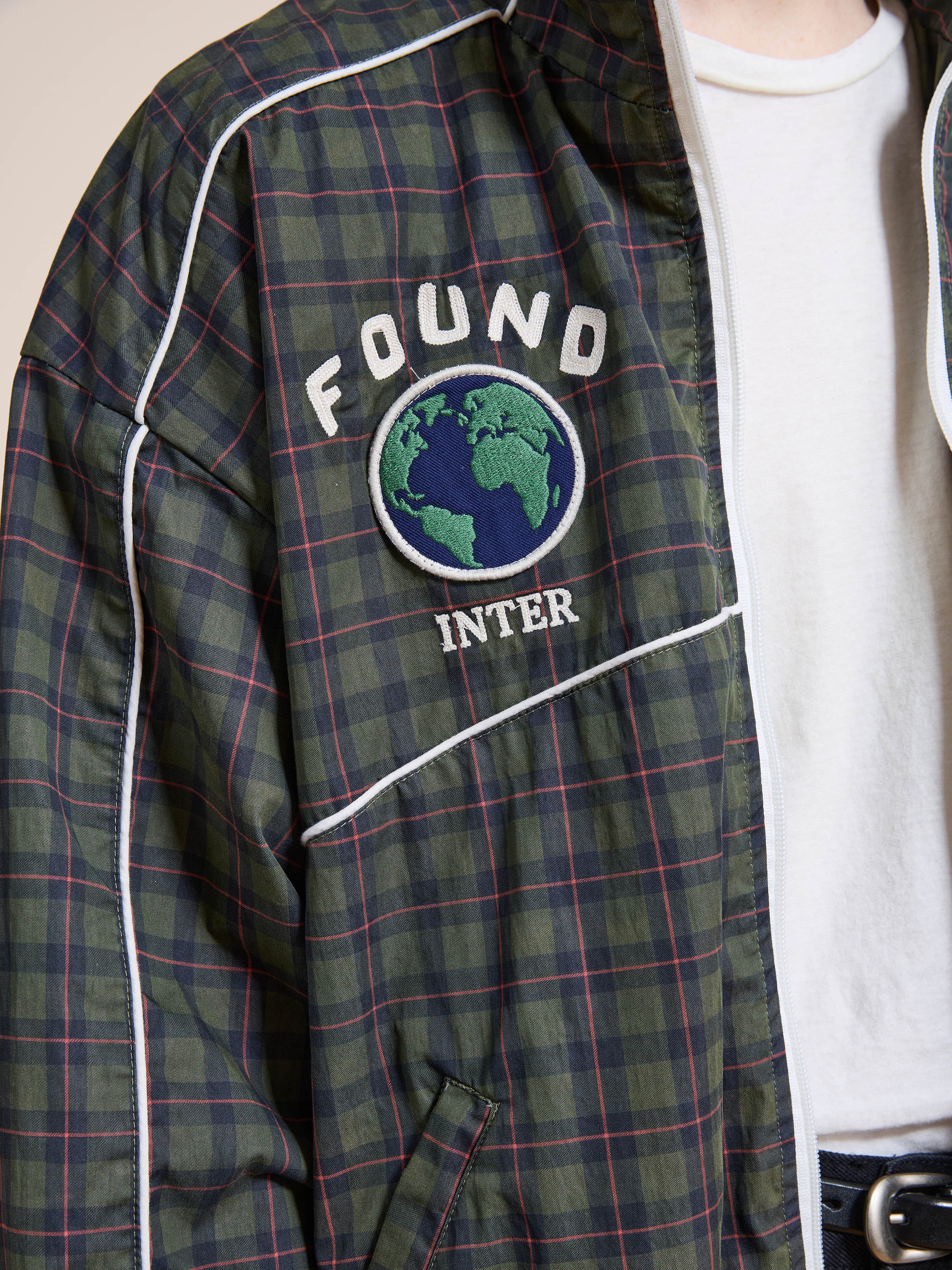 A person wears the FOUND Forest Plaid Track Jacket with white piping, an embroidered globe, and "FOUND" and "INTER" text on the chest.
