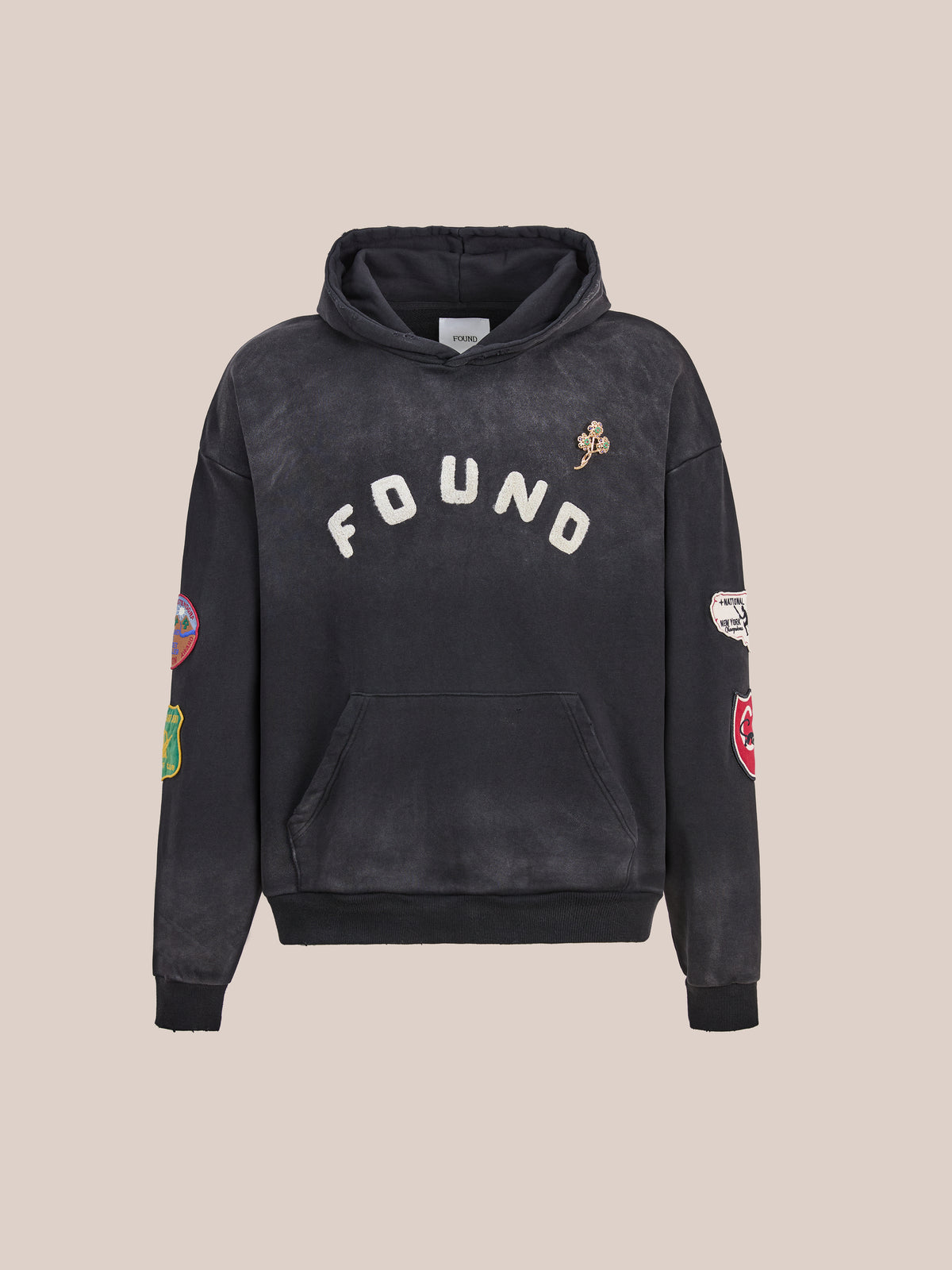 The FOUND Found Logo Patch Hoodie is a black unisex relaxed fit hoodie featuring the word “FOUND” on the chest and several colorful logo patches adorning the sleeves and chest, shown against a plain background.