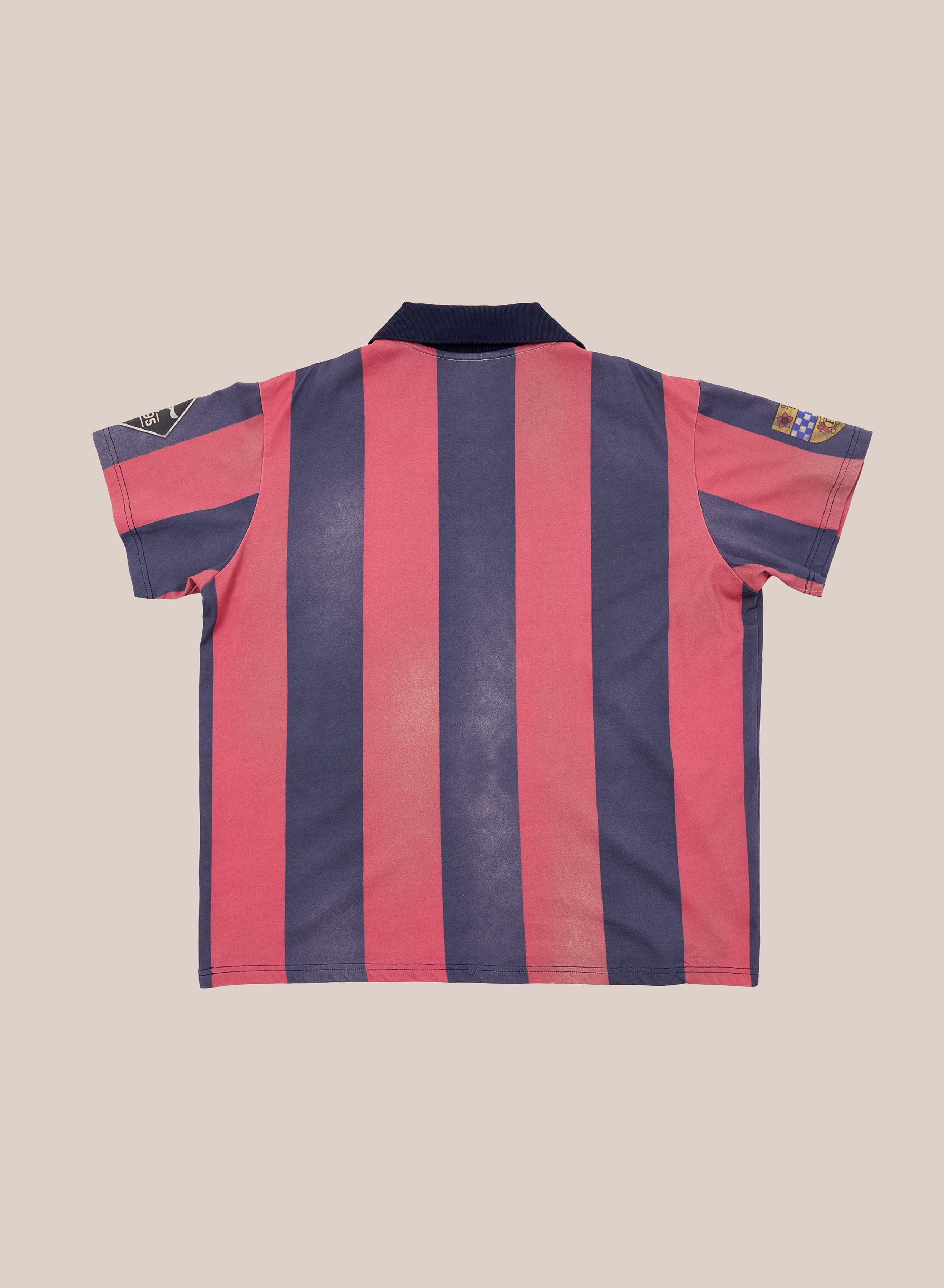 The FOUND Found Club Short Sleeve Jersey is a vintage-inspired unisex top featuring short sleeves, vertical pink and navy blue stripes, a black collar, and sleeve patches. Displayed flat with the back facing up, this relaxed fit club jersey from FOUND blends retro style with everyday comfort.