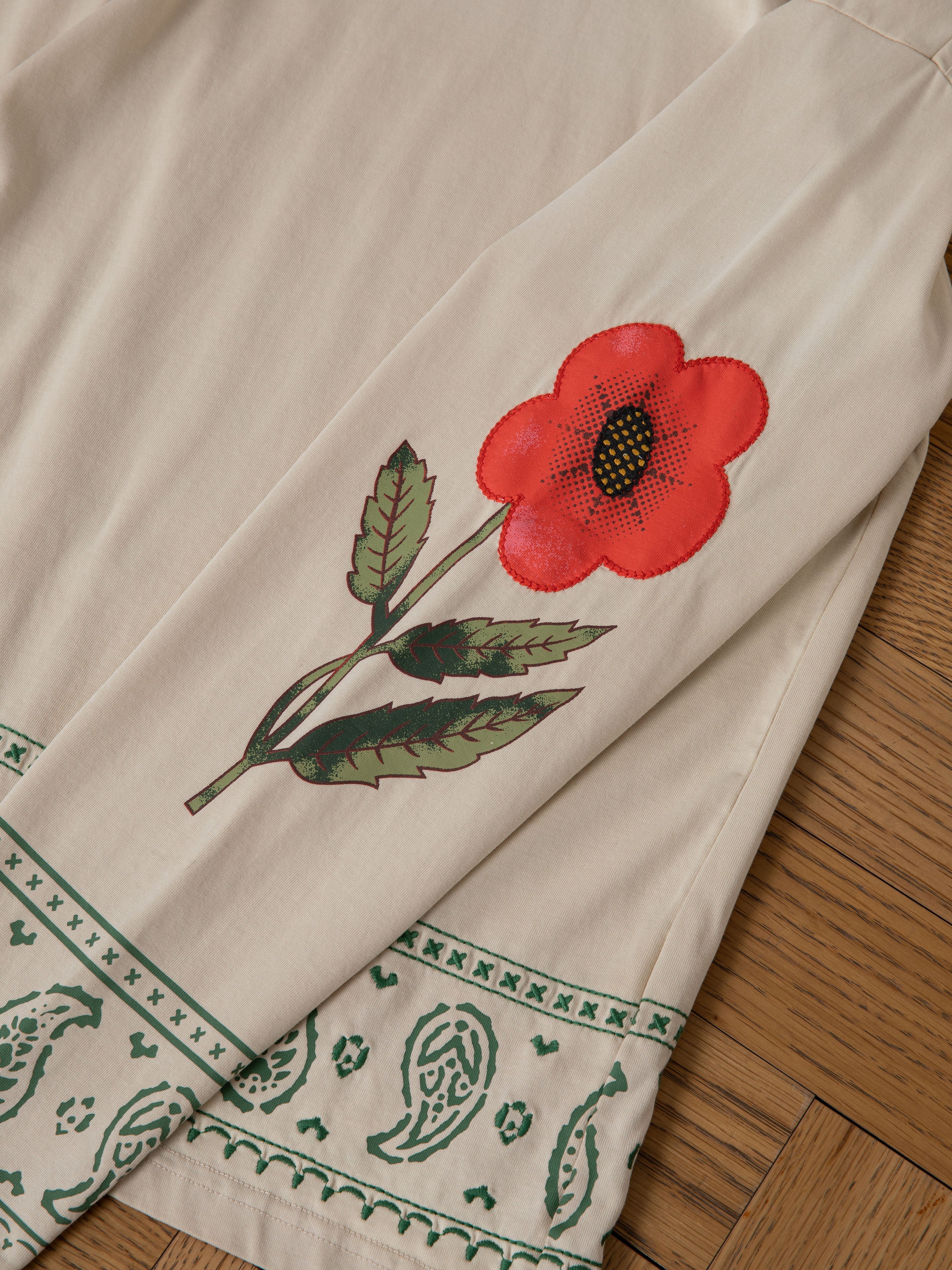 The FOUND Garden Bloom Embroidered LS Tee is a cream-colored, unisex relaxed fit long sleeve with floral embroidery on the sleeve and green paisley and geometric borders near the hem.