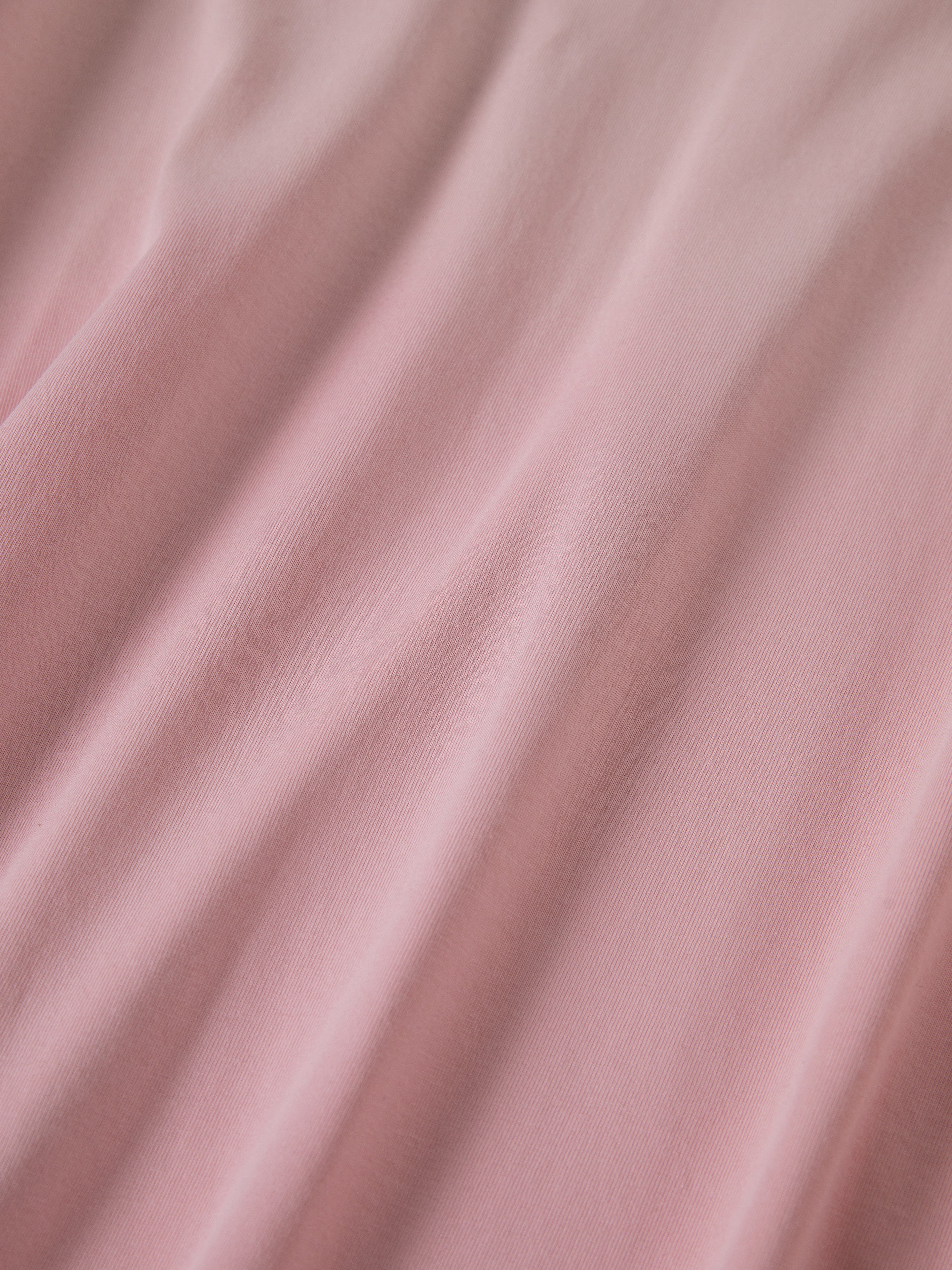 Close-up of light pink fabric from the FOUND Garden Bloom Embroidered LS Tee, a unisex relaxed fit top with soft diagonal folds and visible texture.