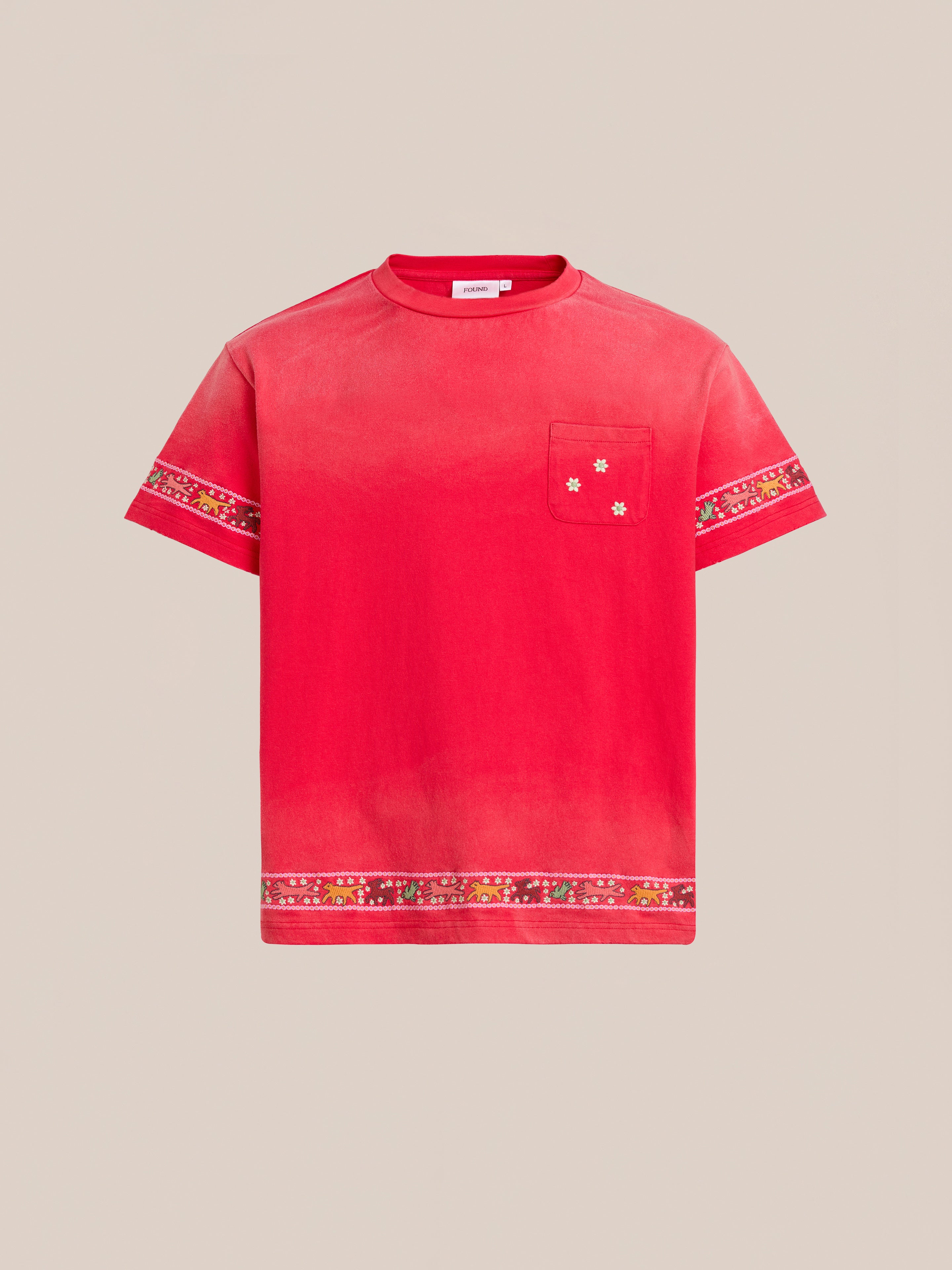 The FOUND Horse Motif Embroidered Tee features a red vintage wash, short sleeves, chest pocket, floral accents, and decorative patterned bands on the sleeves and hem, shown against a plain beige background.