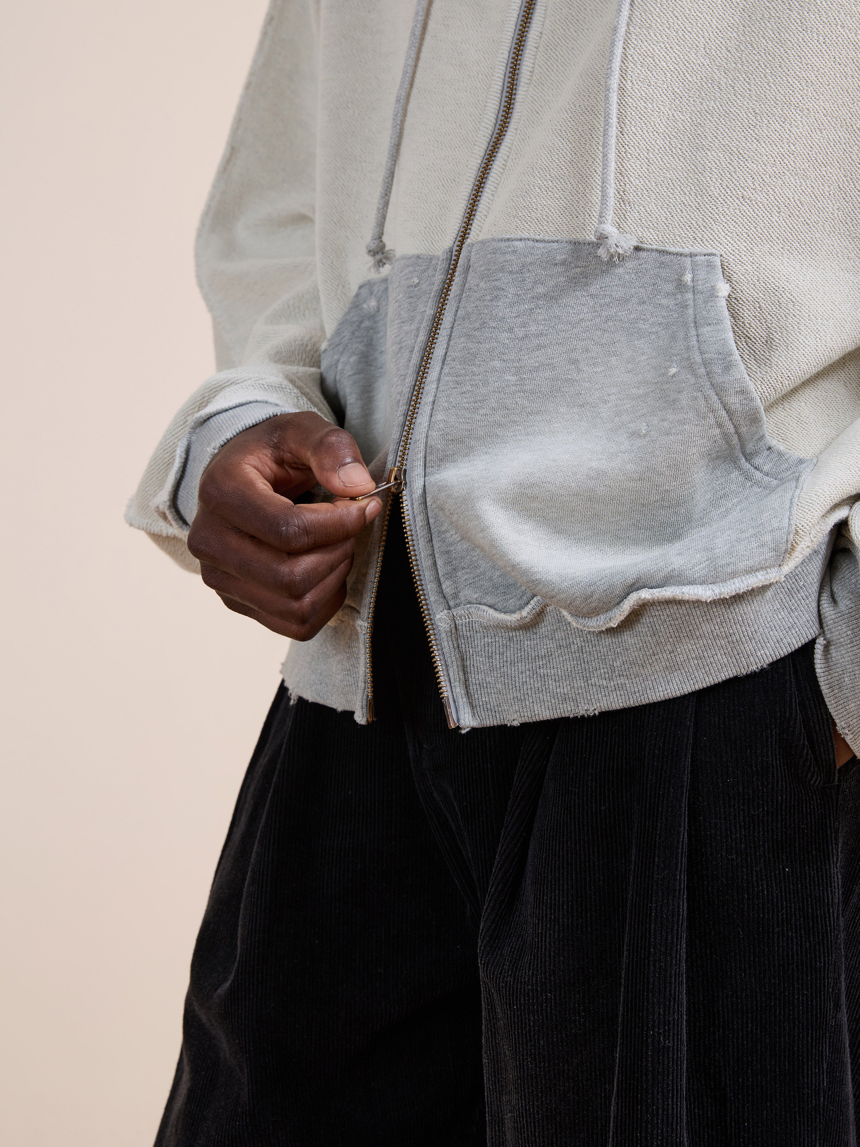 Someone wearing the FOUND Deconstructed Terry Zip Up Hoodie in light gray and dark pants is zipping up the front of the hoodie.
