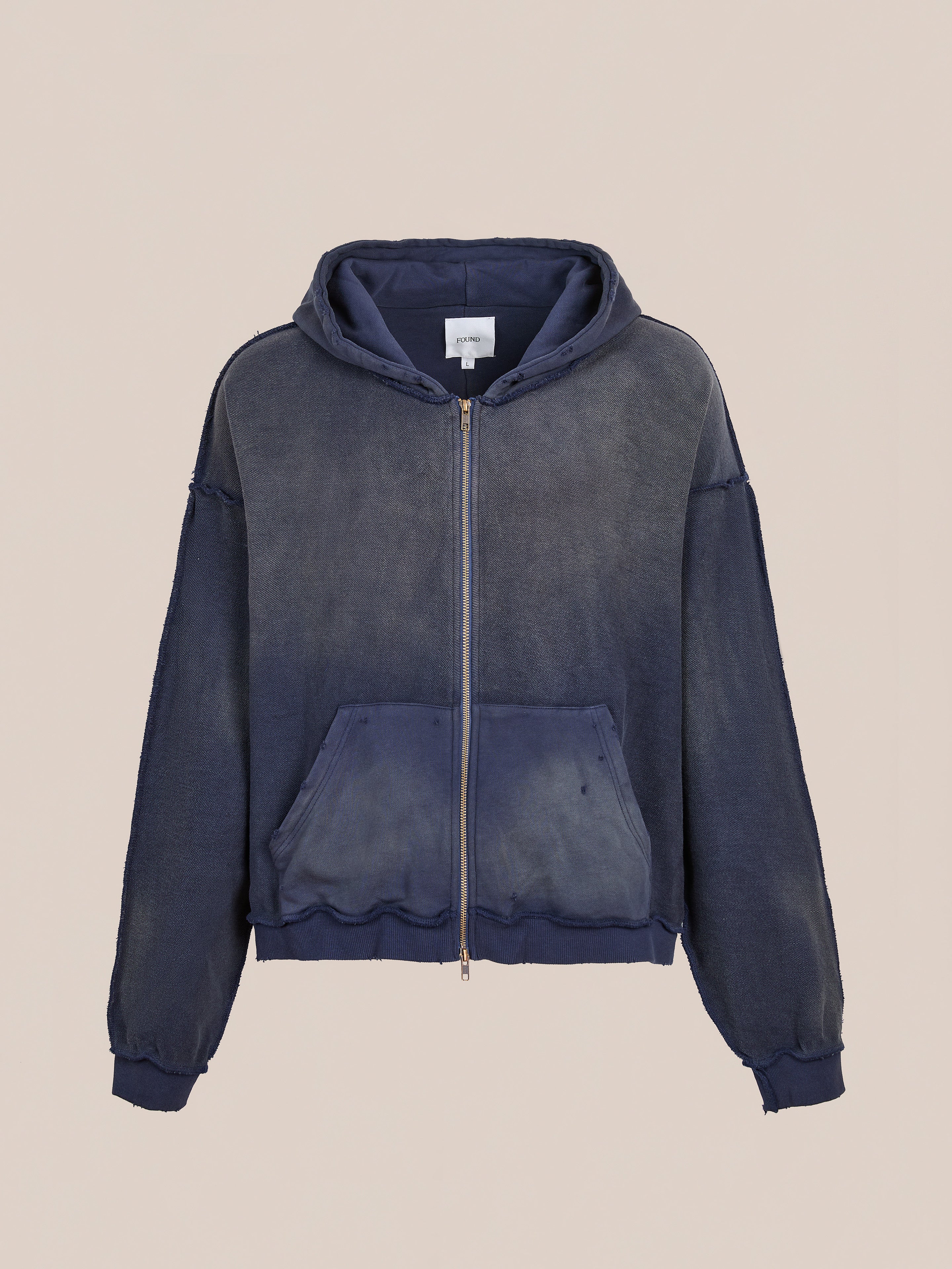 The FOUND Deconstructed Terry Zip Up Hoodie in faded navy blue features a relaxed fit, front kangaroo pocket, ribbed cuffs, and a hood, shown on a plain beige background.