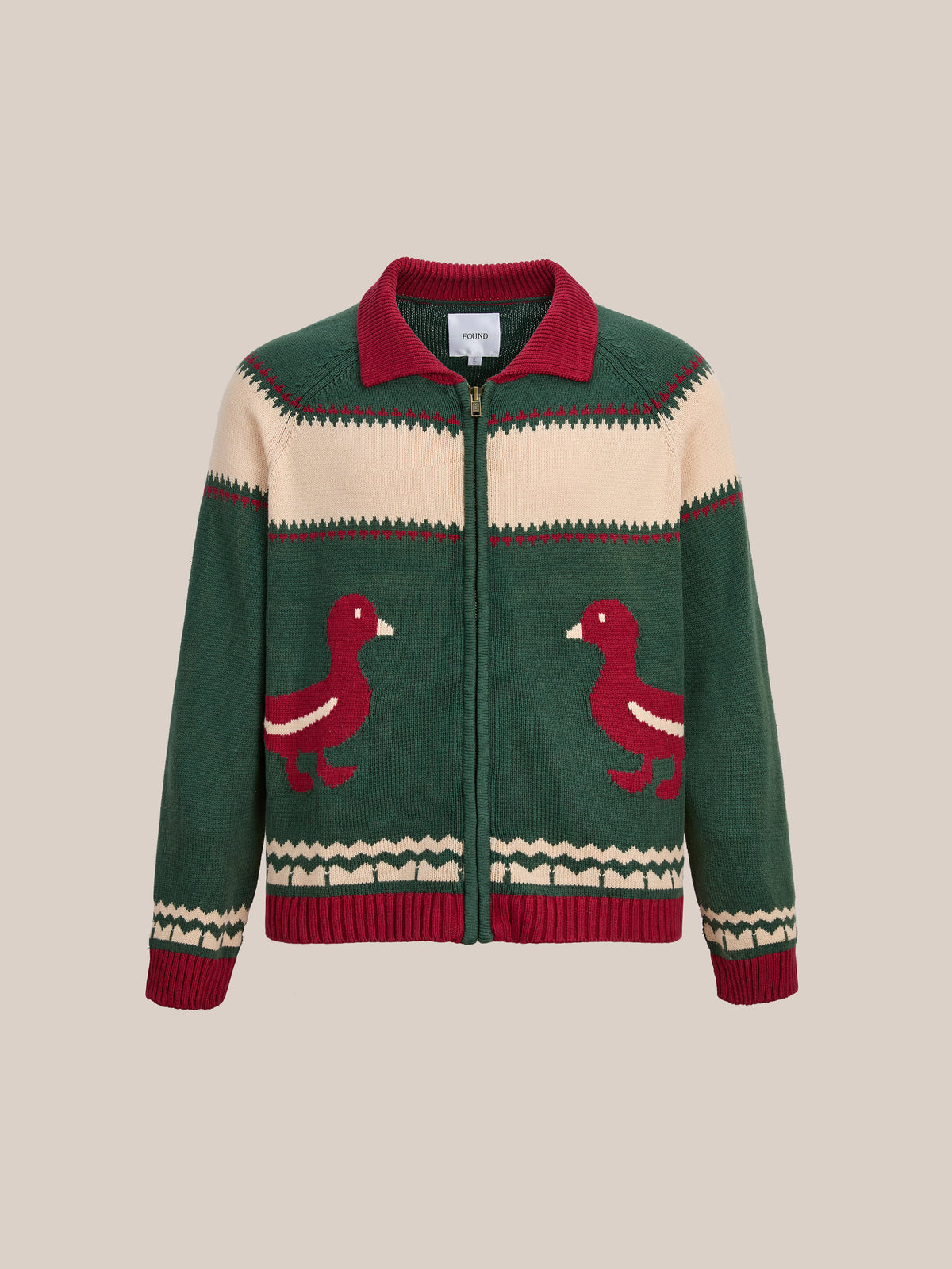 The FOUND Isles Sweater features green and cream hues with red duck motifs and geometric patterns, blending vintage knitwear style with modern appeal.