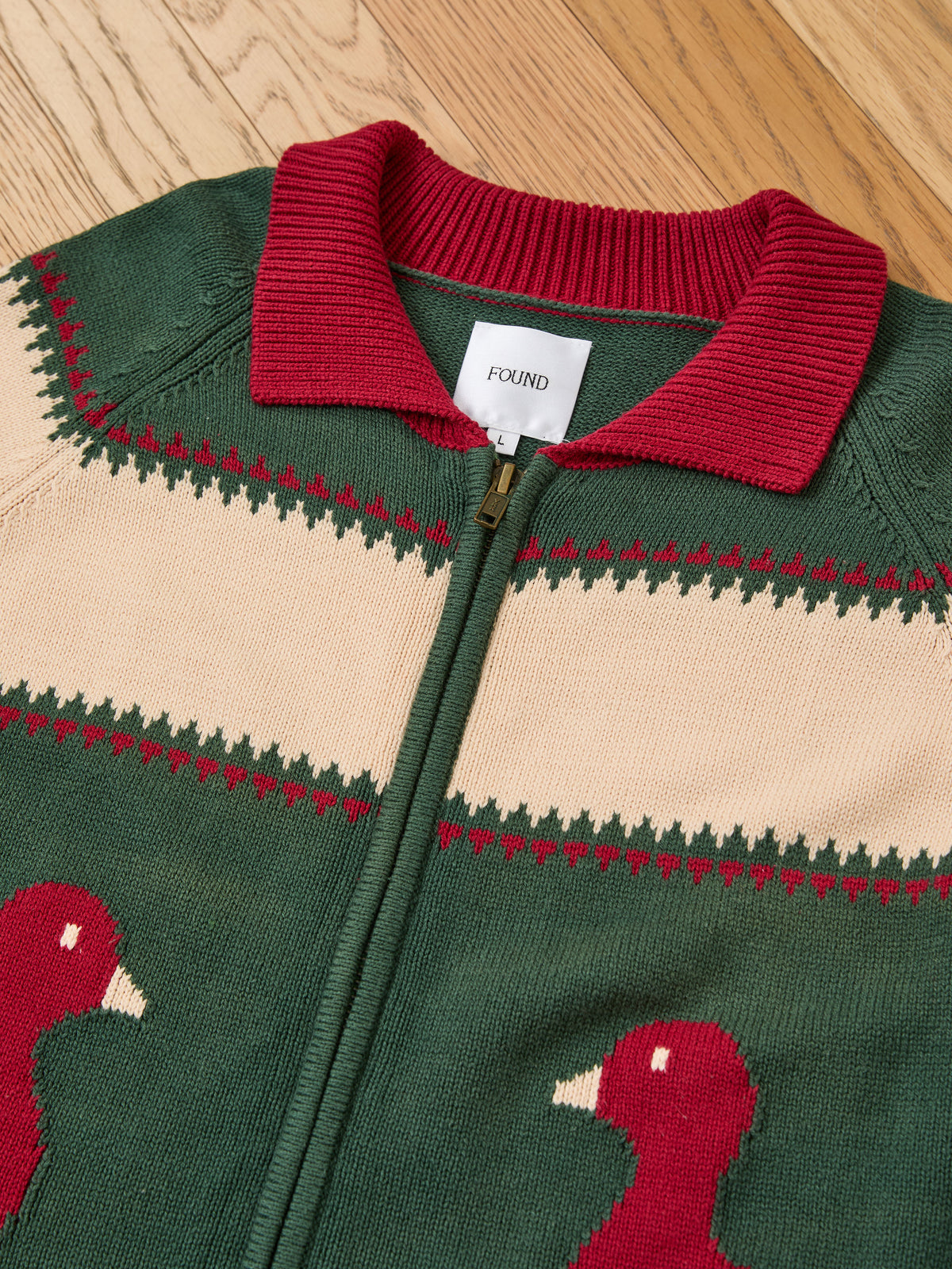 FOUND Isles Sweater—vintage unisex knit with red collar, cream stripe, and red bird pattern, shown flat on wood. Label reads “FOUND.”.