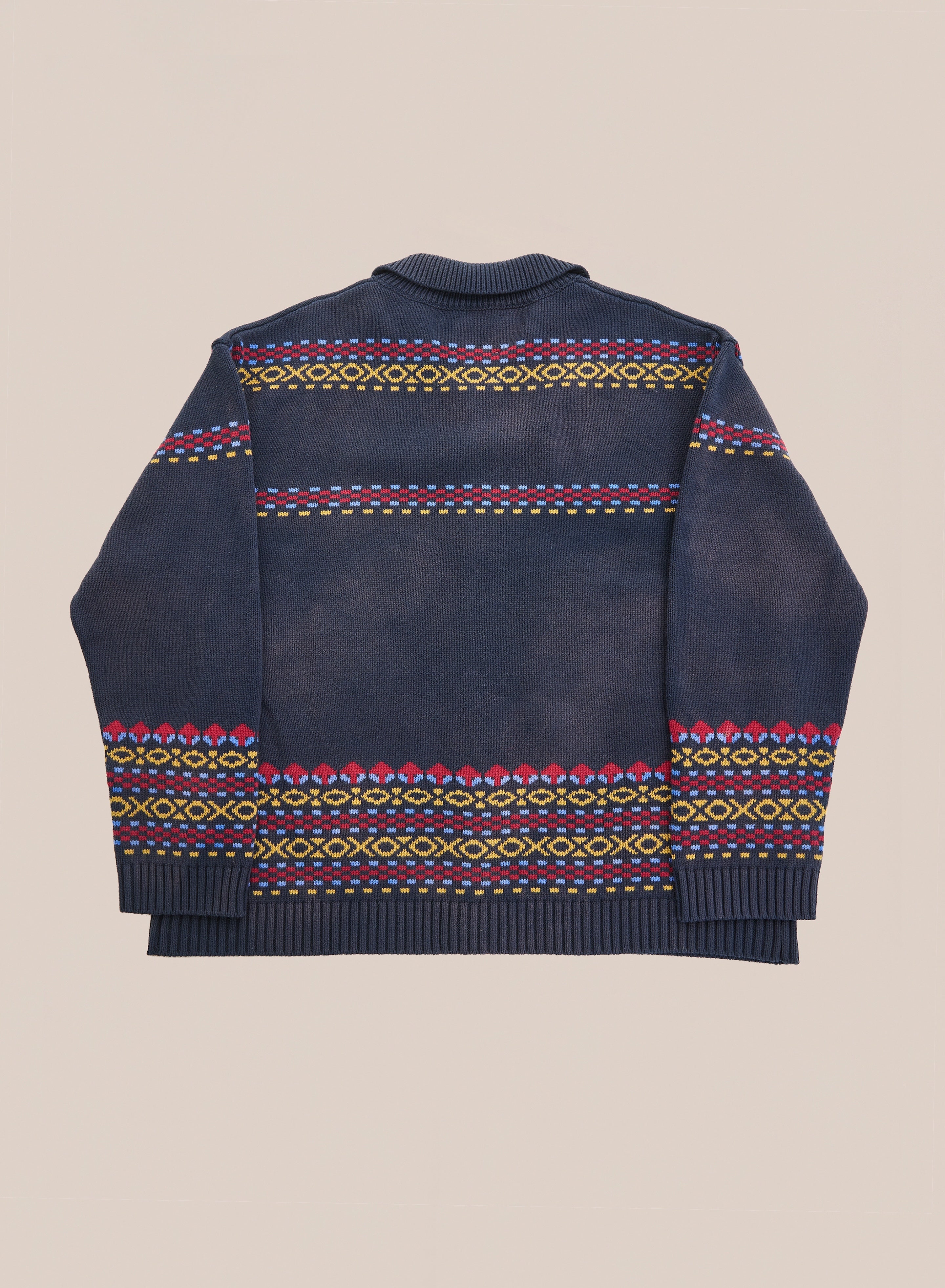 The Isles Sweater by Found, a navy knit featuring vibrant geometric patterns in yellow, pink, and green along the back, hem, and cuffs—plus understated jacquard horse motifs—is shown laid flat on a neutral backdrop.