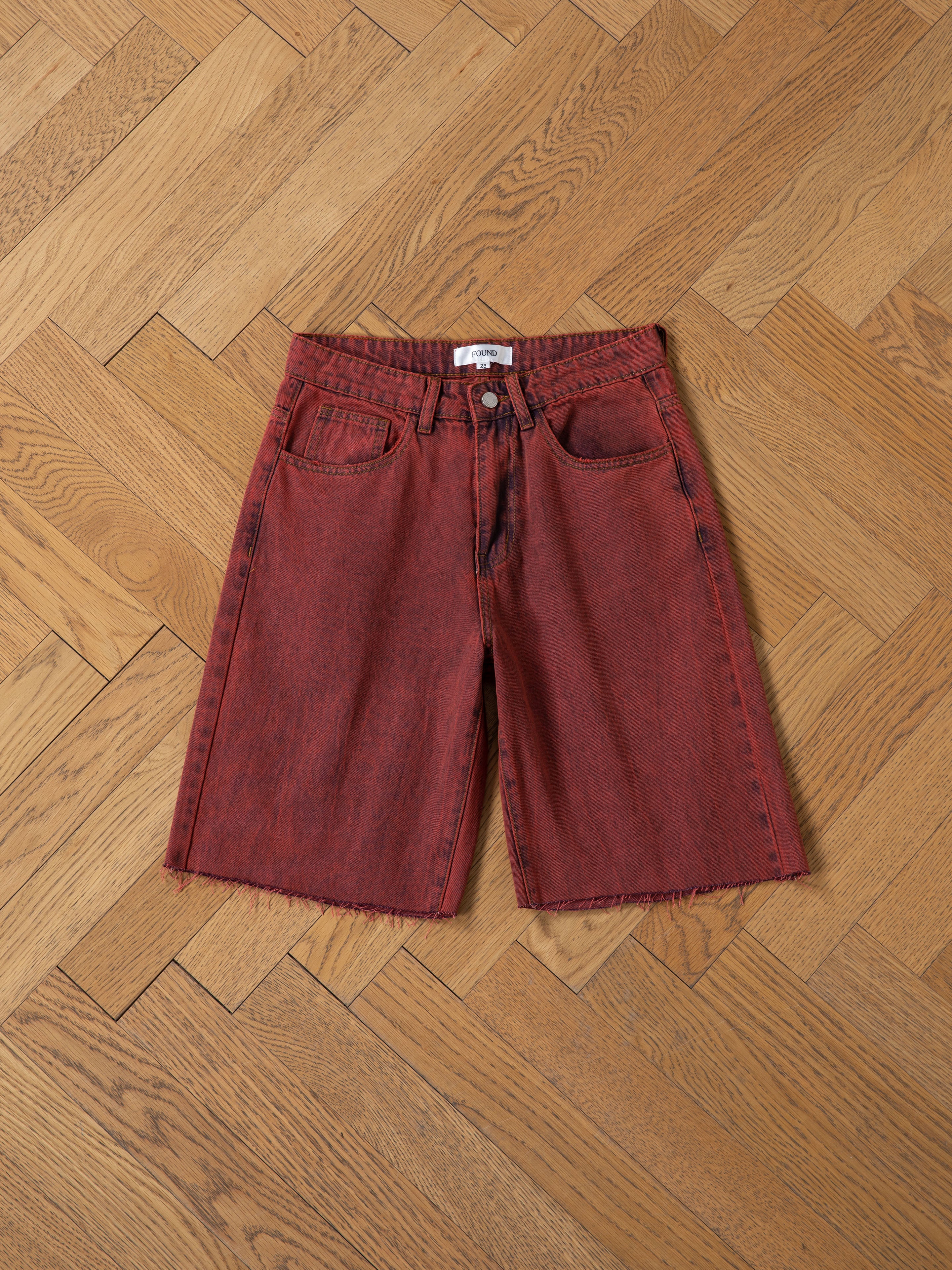 FOUND Lacy Jean Jorts: 100% cotton vintage red denim shorts with frayed hem, five pockets, and button closure, shown laid flat on a light wood herringbone floor.