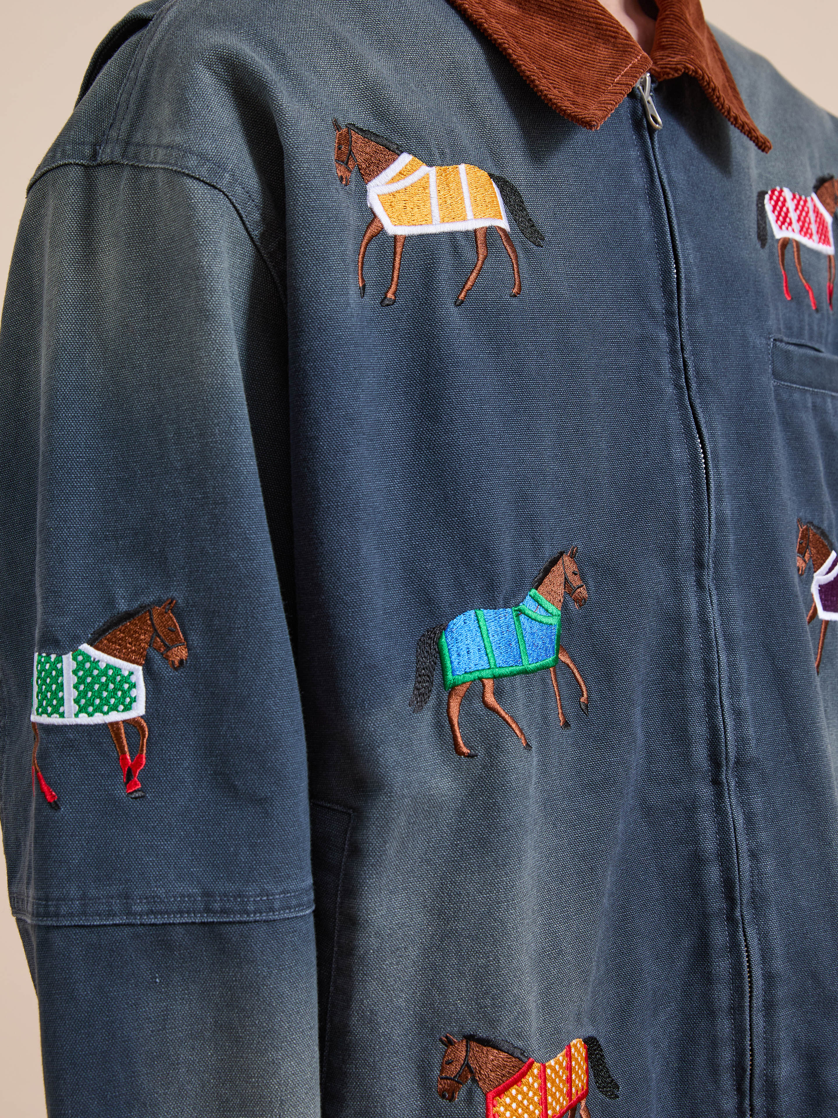 Close-up of the Found Lariat Horse Embroidered Work Jacket, a unisex navy piece with colorful horse embroidery, brown collar, and front zipper.