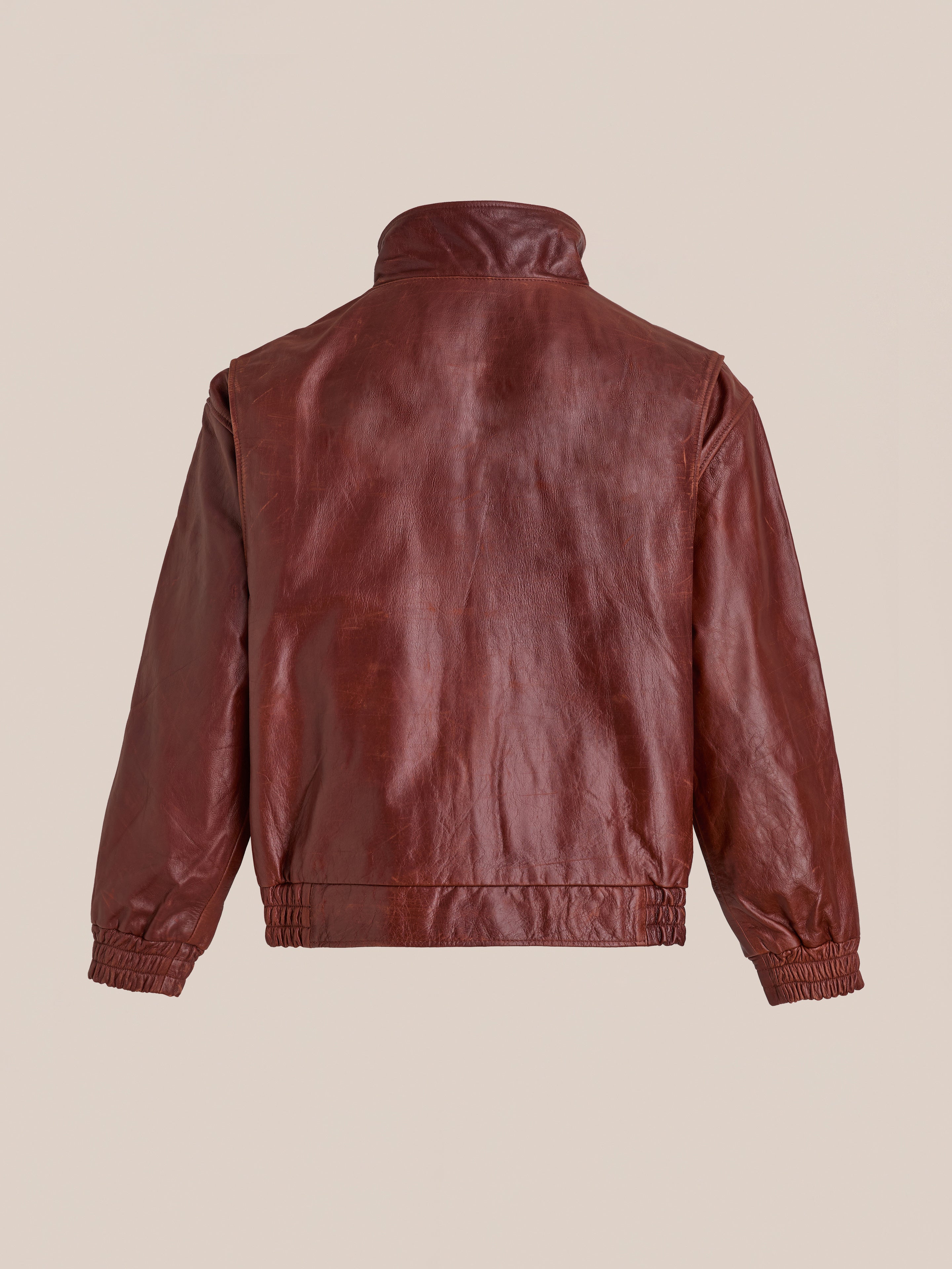 The Found Redwood Leather Bomber Jacket is shown from the back, featuring a high collar, elastic cuffs, and waistband, all set against a plain beige background.