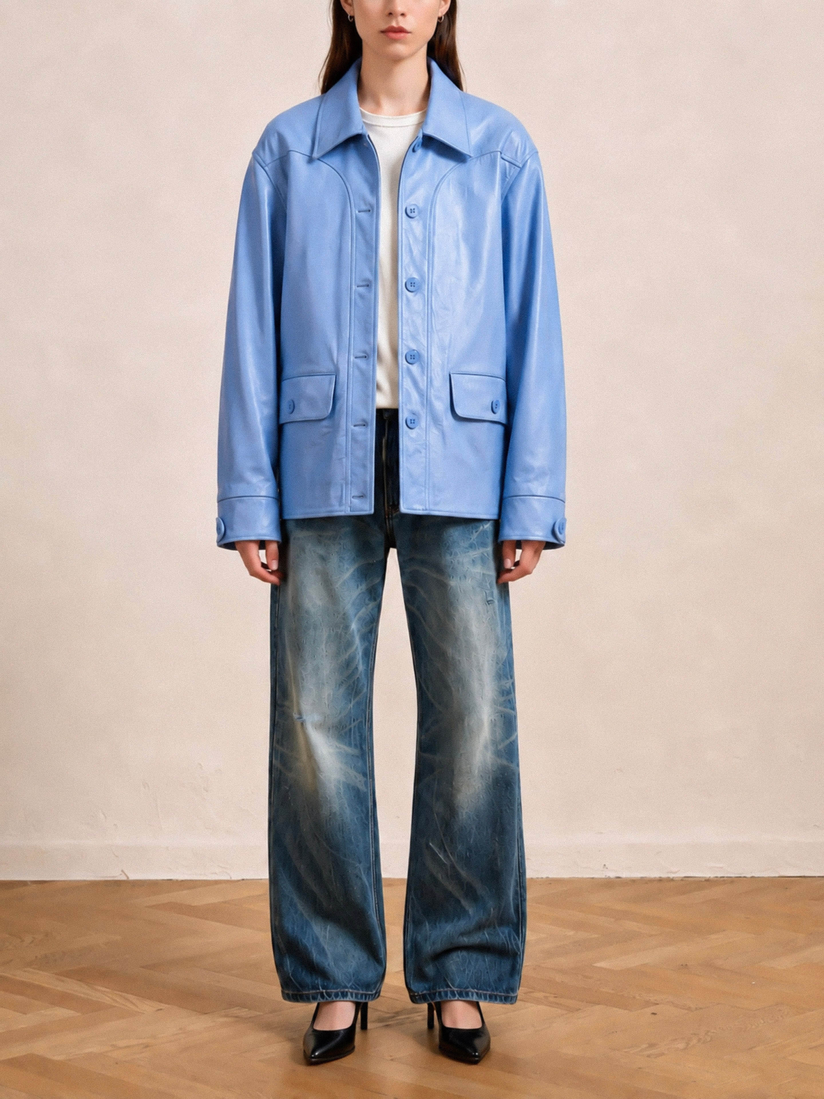 A person wearing the FOUND Leather Field Jacket in light blue, a white shirt, relaxed fit wide-leg faded jeans, and black heels stands on a wooden floor against a plain beige wall.