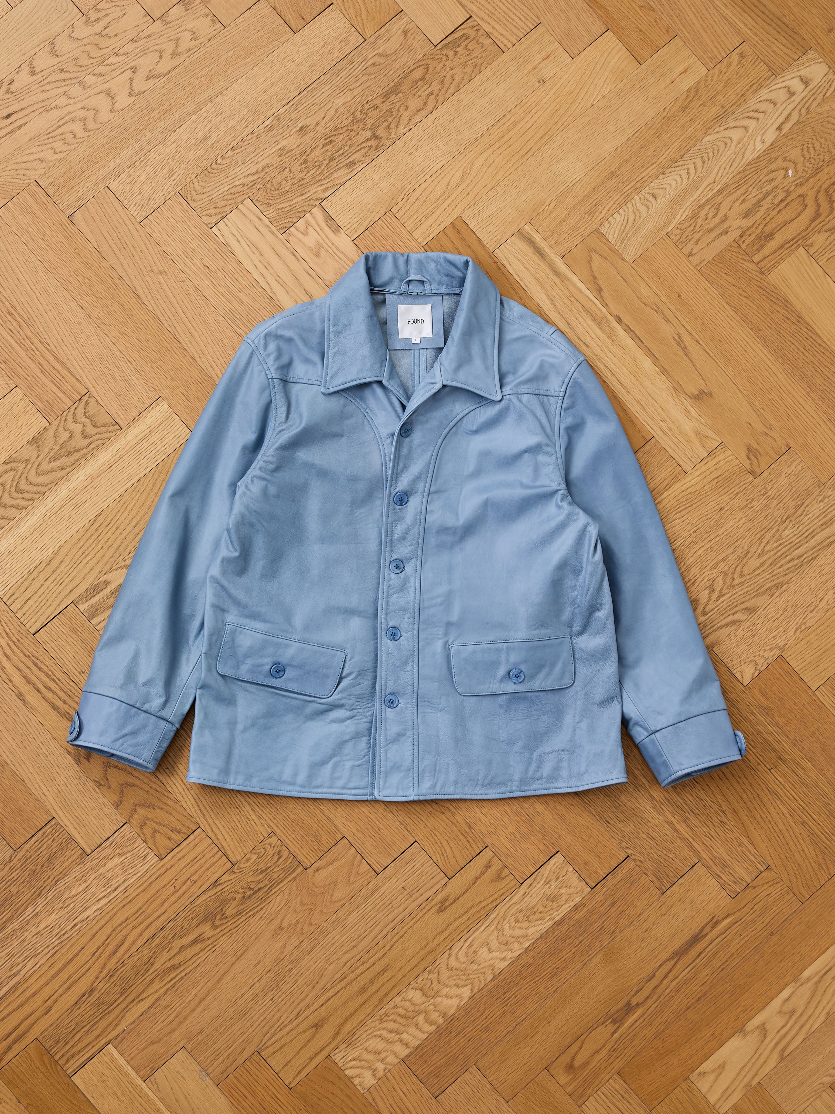 FOUND Leather Field Jacket with a collar and two front pockets, unisex relaxed fit, laid flat on a wooden herringbone-patterned floor.