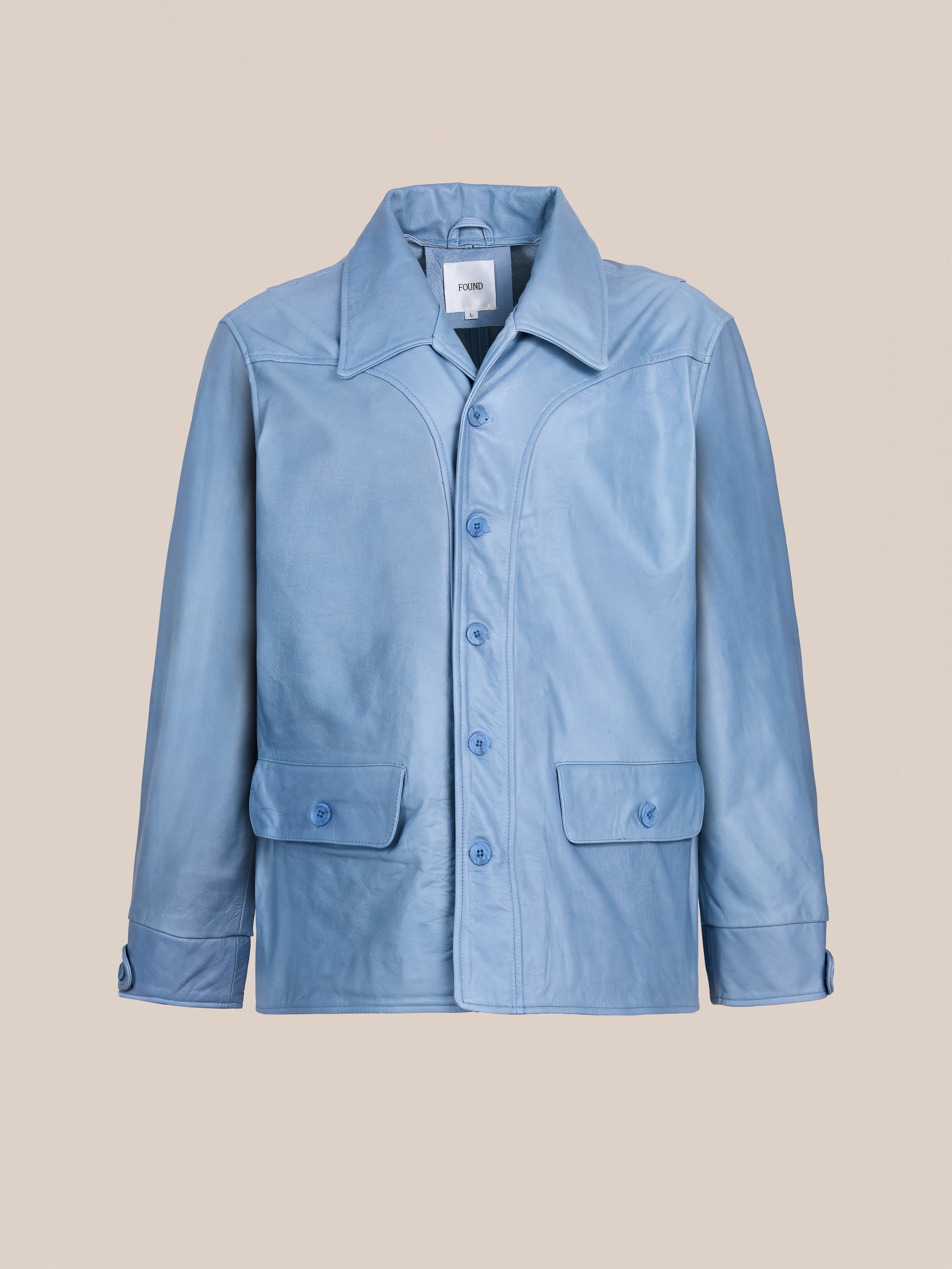 The FOUND Leather Field Jacket is a light blue unisex style with a relaxed fit, wide collar, front flap pockets, and matching blue buttons, shown against a plain beige background.