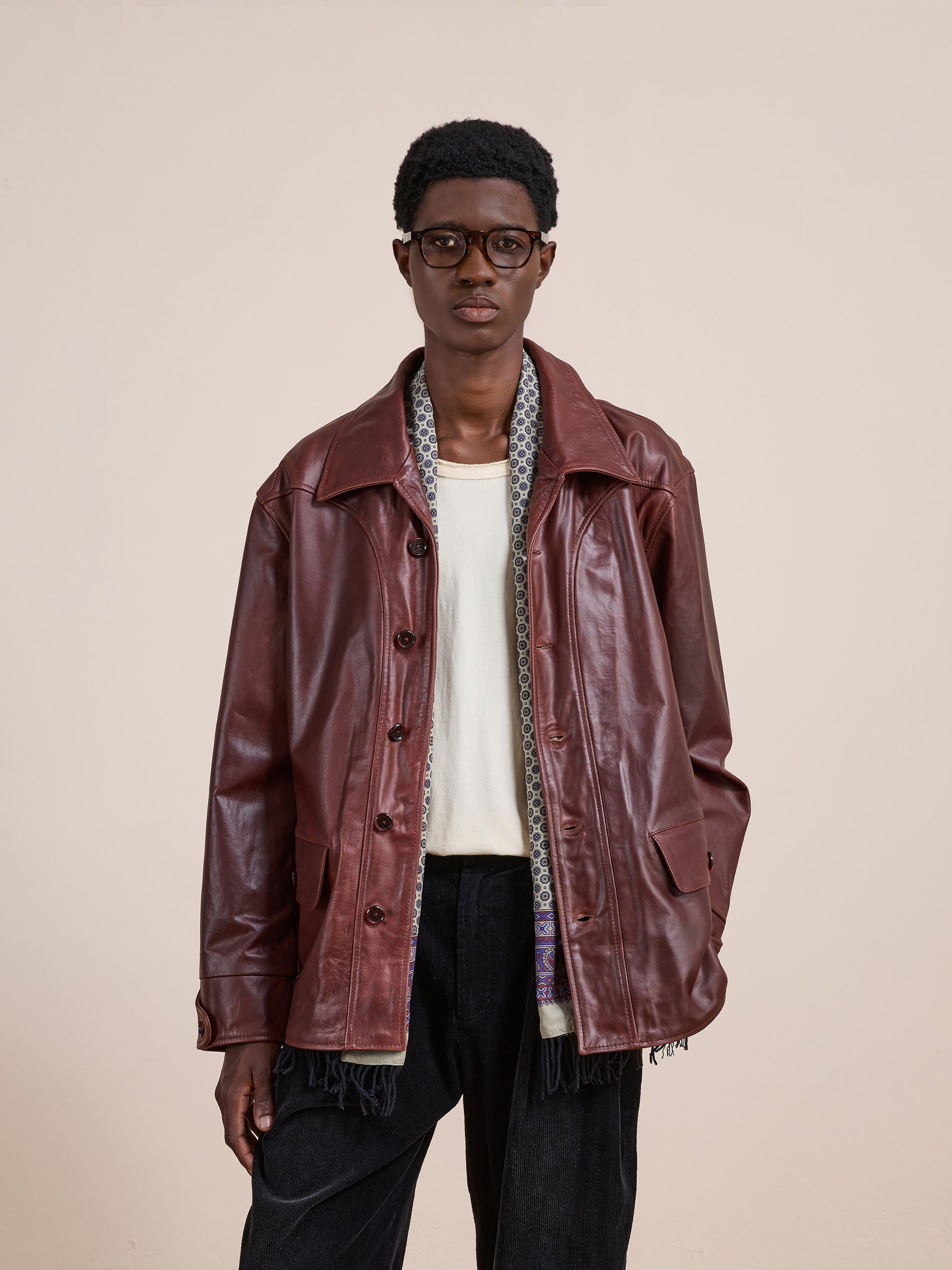 A person wearing the FOUND Leather Field Jacket in a unisex relaxed fit, styled with a white shirt, black pants, and glasses stands against a plain light background.