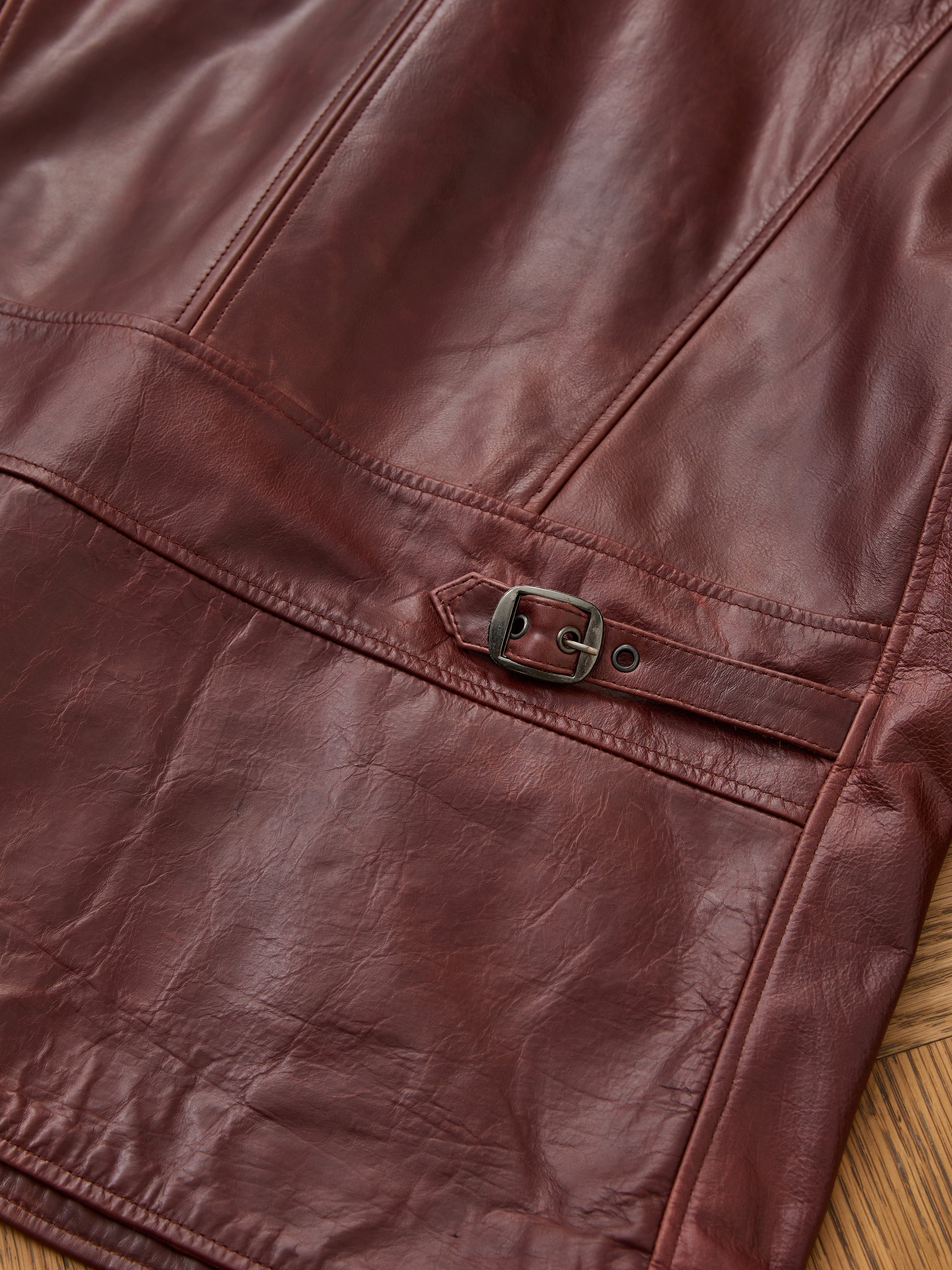 Close-up of the FOUND Leather Field Jacket, a unisex brown leather piece featuring a side strap with metal buckle and visible stitching, designed for a relaxed fit.