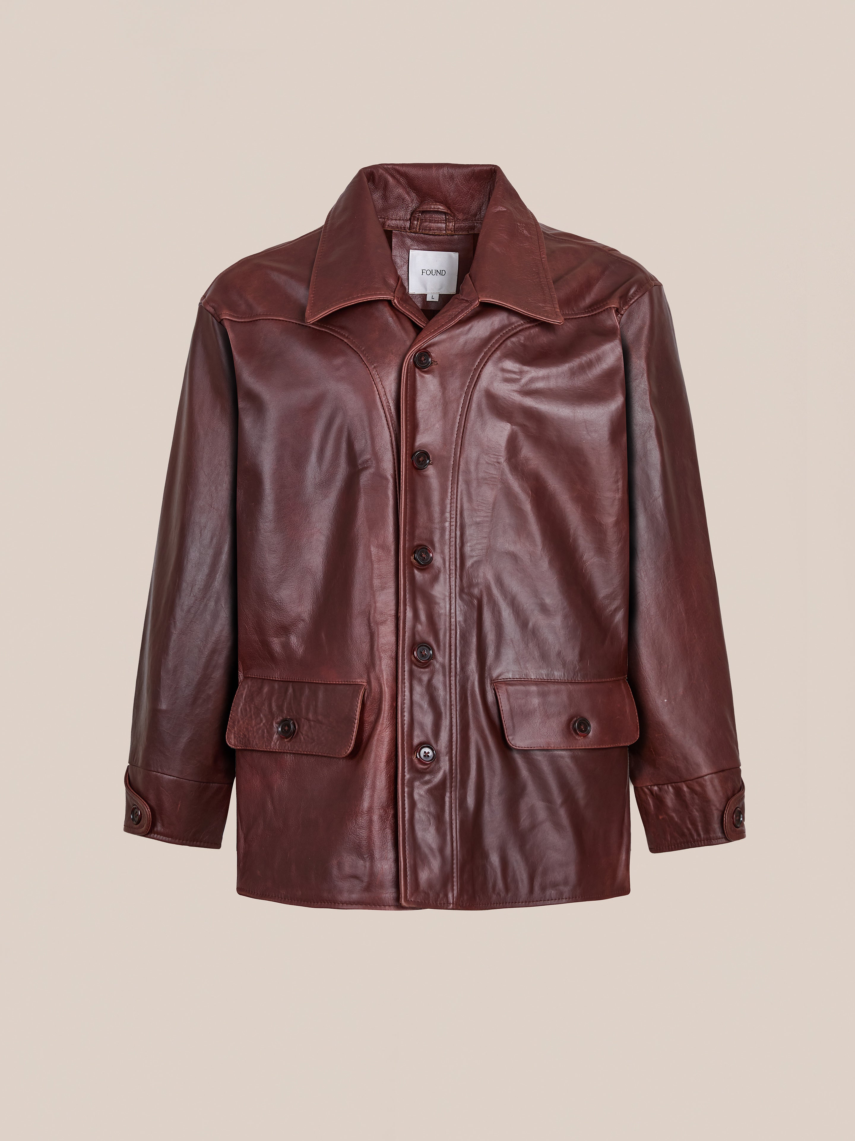 The FOUND Leather Field Jacket features a relaxed fit, brown leather, collar, two front flap pockets, and buttoned cuffs, shown against a plain beige background.