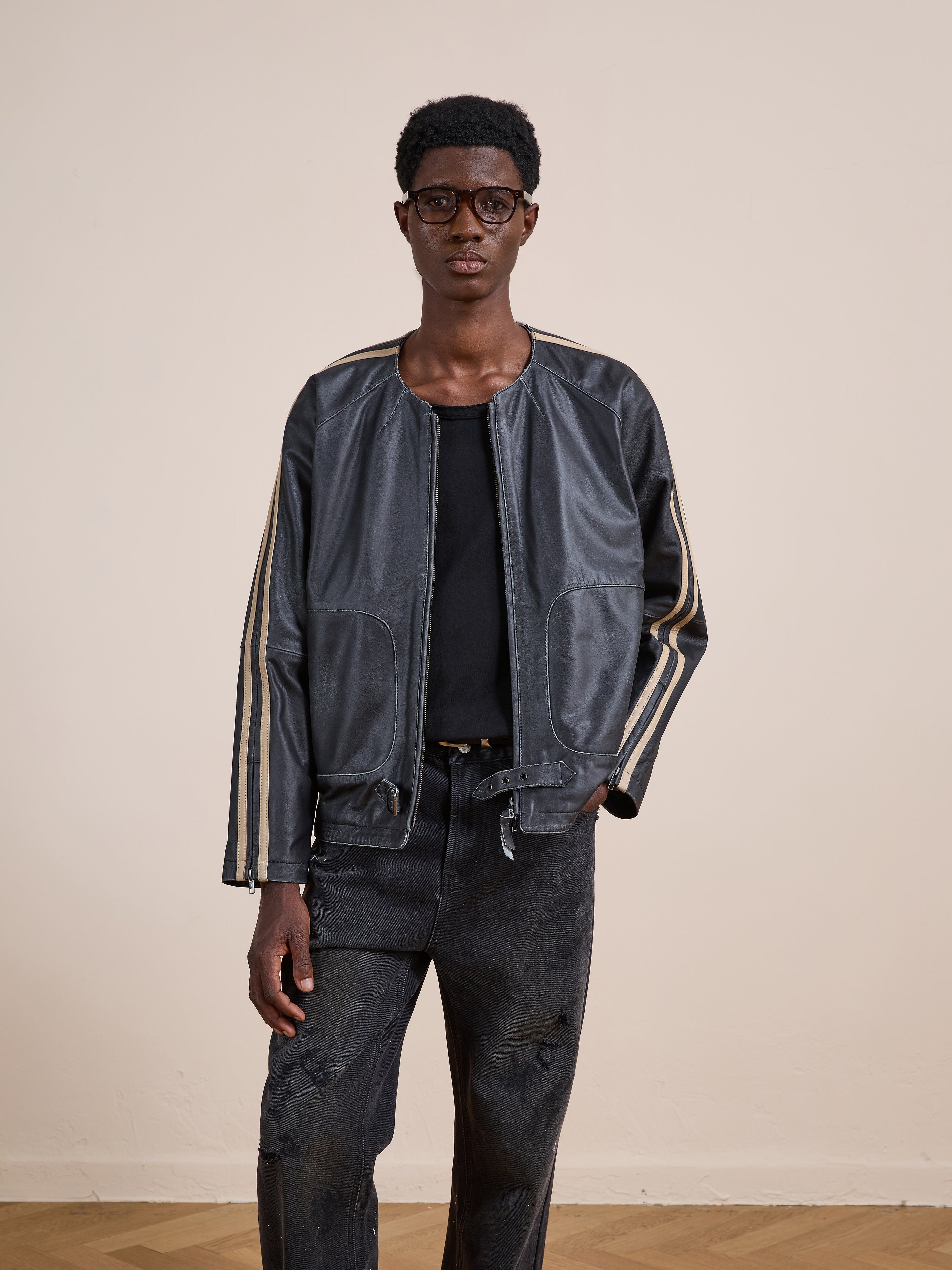 A person wears the FOUND Leather Track Jacket with beige sleeve stripes, a black shirt, and dark jeans, standing against a plain beige background.