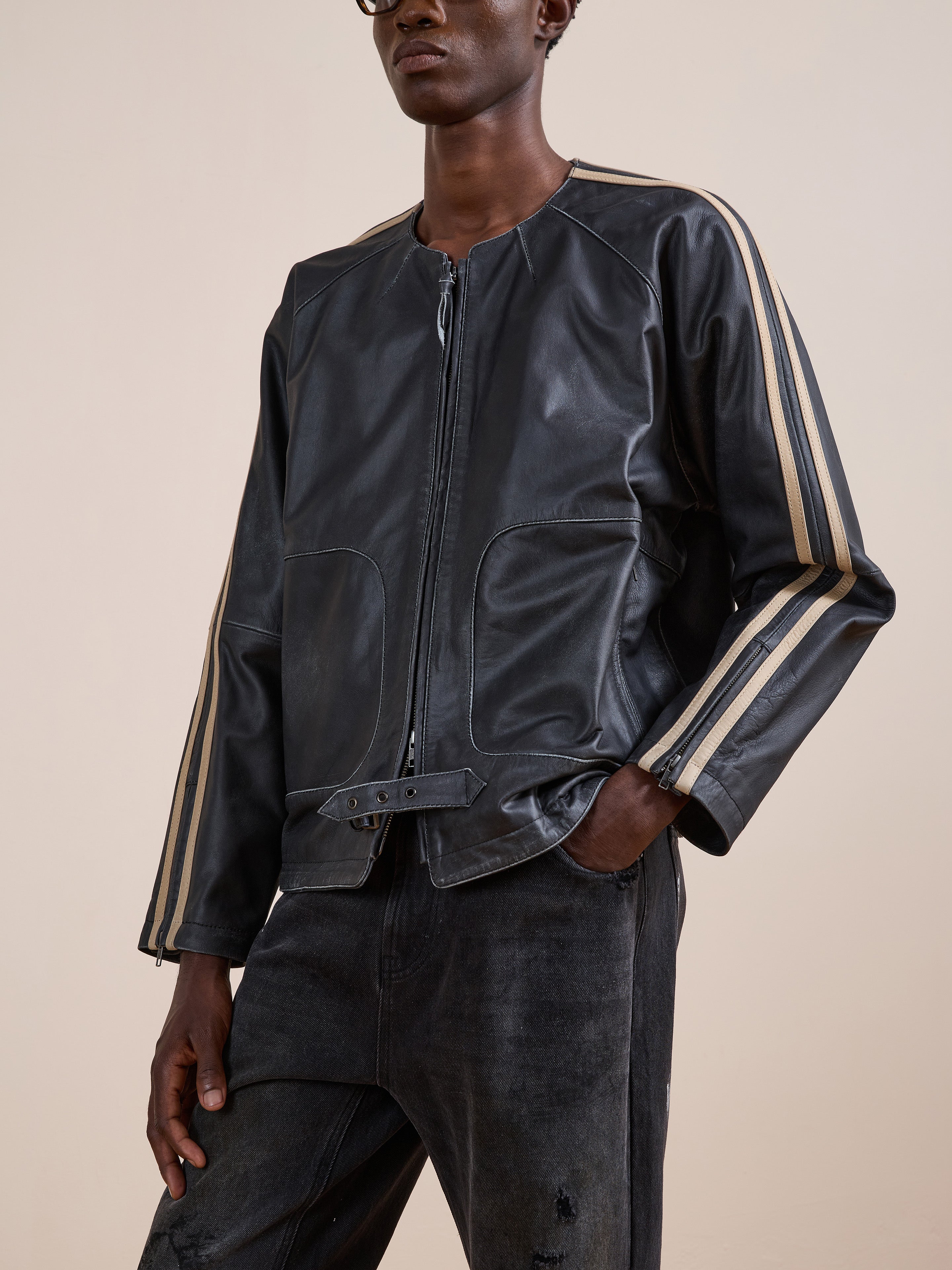 A person wearing the FOUND Leather Track Jacket with beige sleeve stripes and dark jeans stands against a plain background.