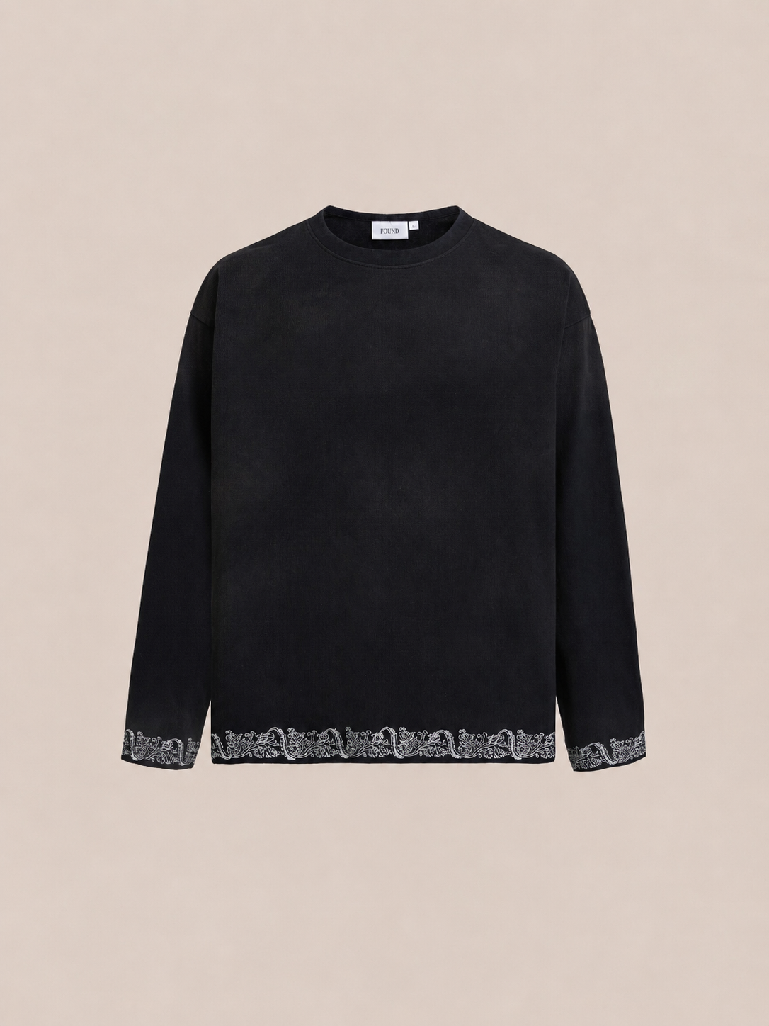 The FOUND Metallic Long Sleeve Embroidered Tee features a unisex relaxed fit, crew neck, and subtle metallic embroidery along the cuffs and hem, displayed on a plain beige background.