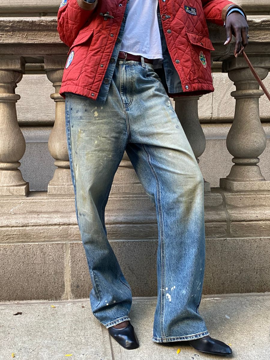 A person in a red jacket and white shirt stands by a stone railing in Monet Paint Jeans by FOUND.