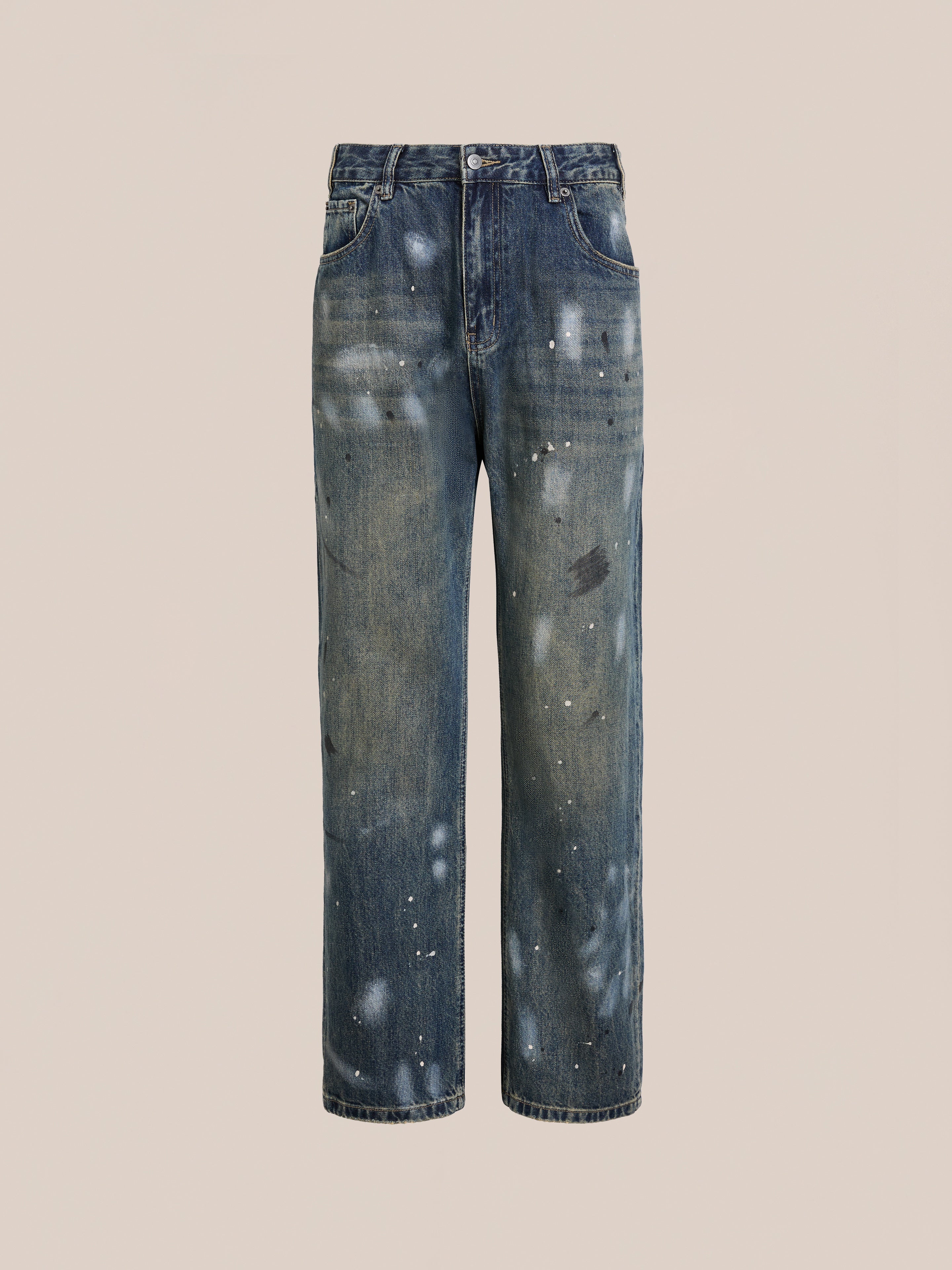 The FOUND Monet Paint Jeans are straight-leg, vintage blue jeans with a distressed, paint-splattered finish, front and back pockets, a button fly, and a unisex relaxed fit. Shown on a plain beige background.