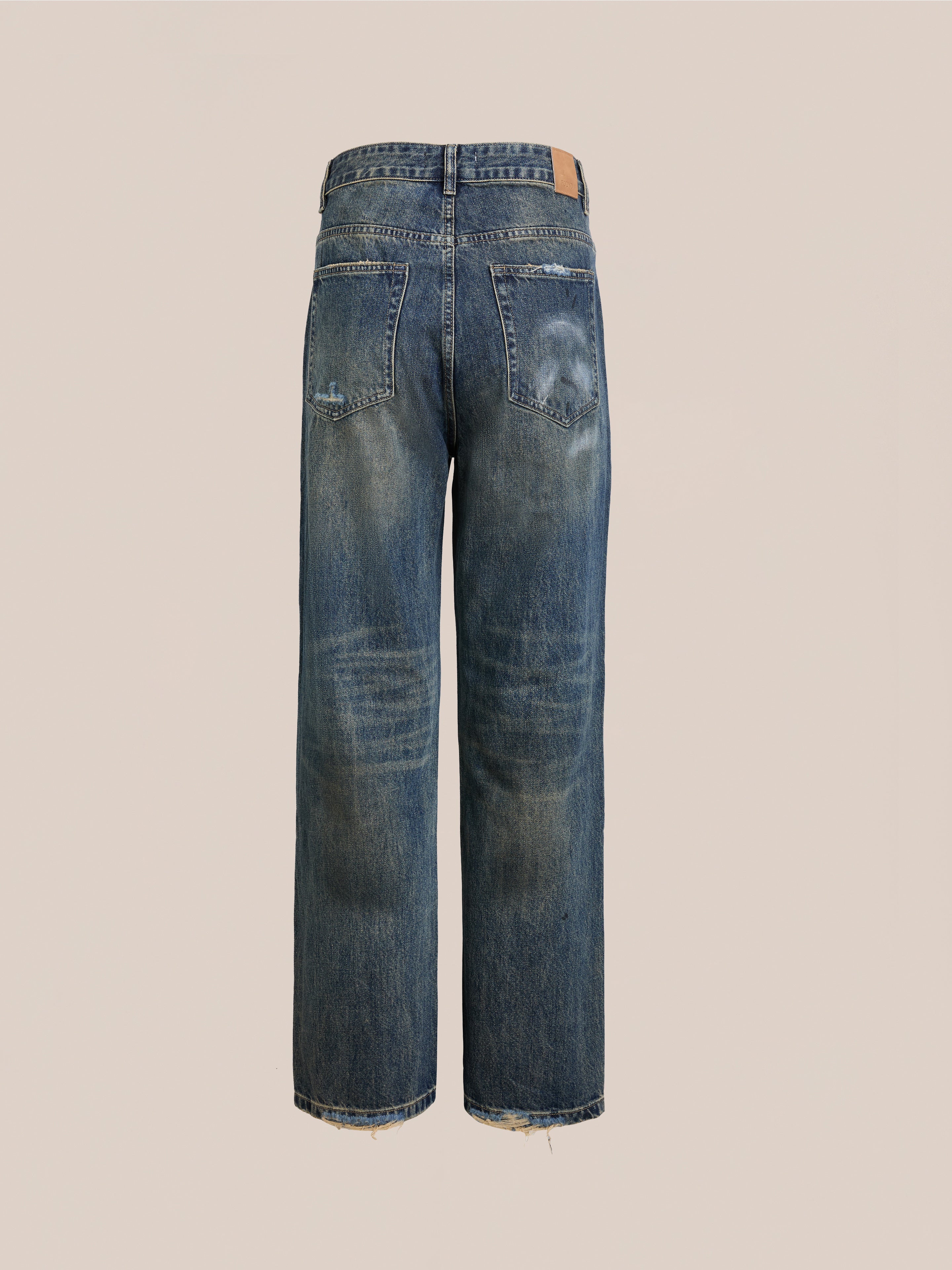 Back view of FOUND Monet Paint Jeans in vintage blue with visible fading, frayed hems, and a brown waistband patch. Unisex relaxed fit shown against a plain background.