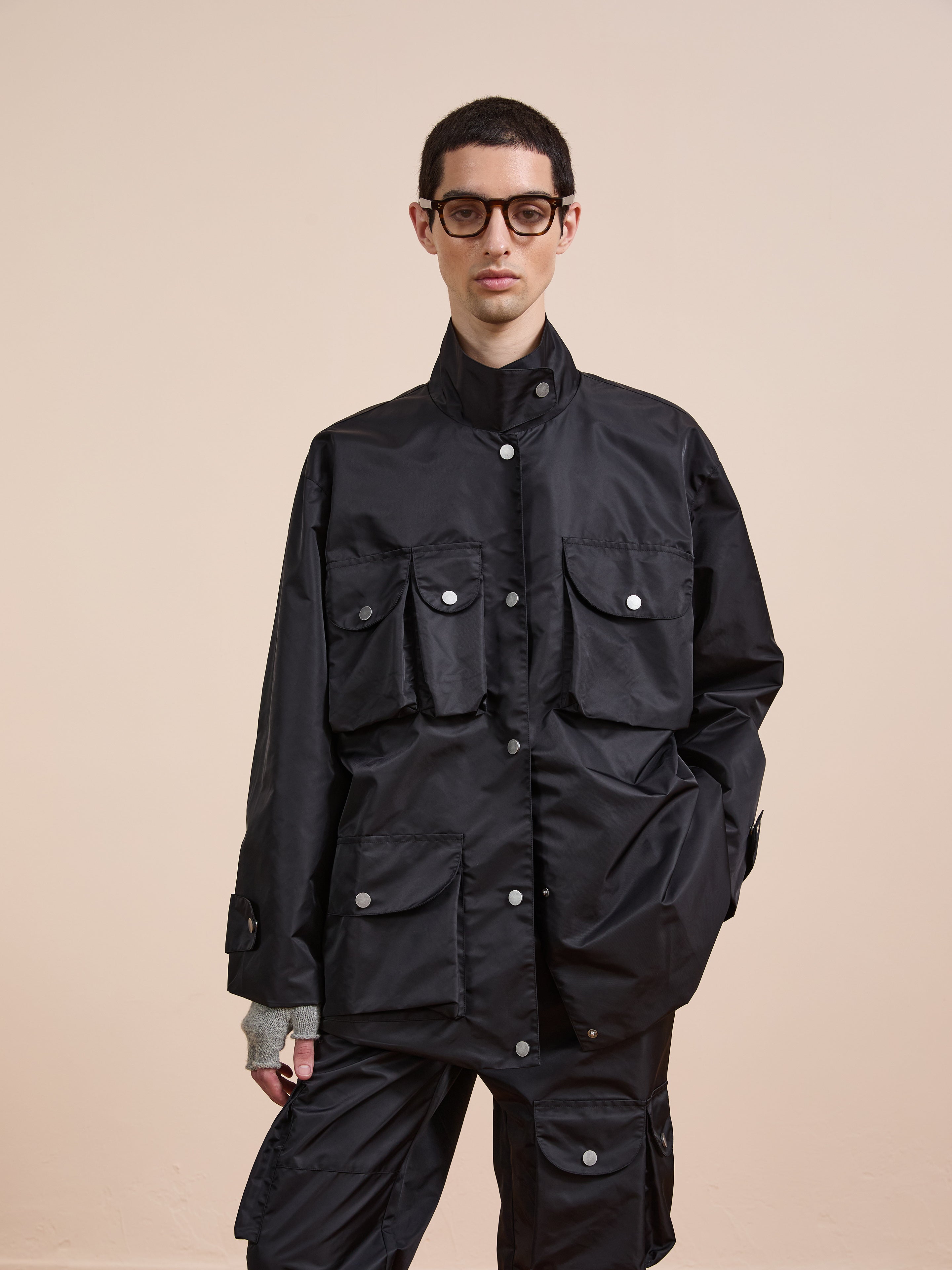 Model wears the FOUND Cargo Nylon Jacket—an oversized black jacket with multiple front pockets—paired with black pants, set against a plain beige background.