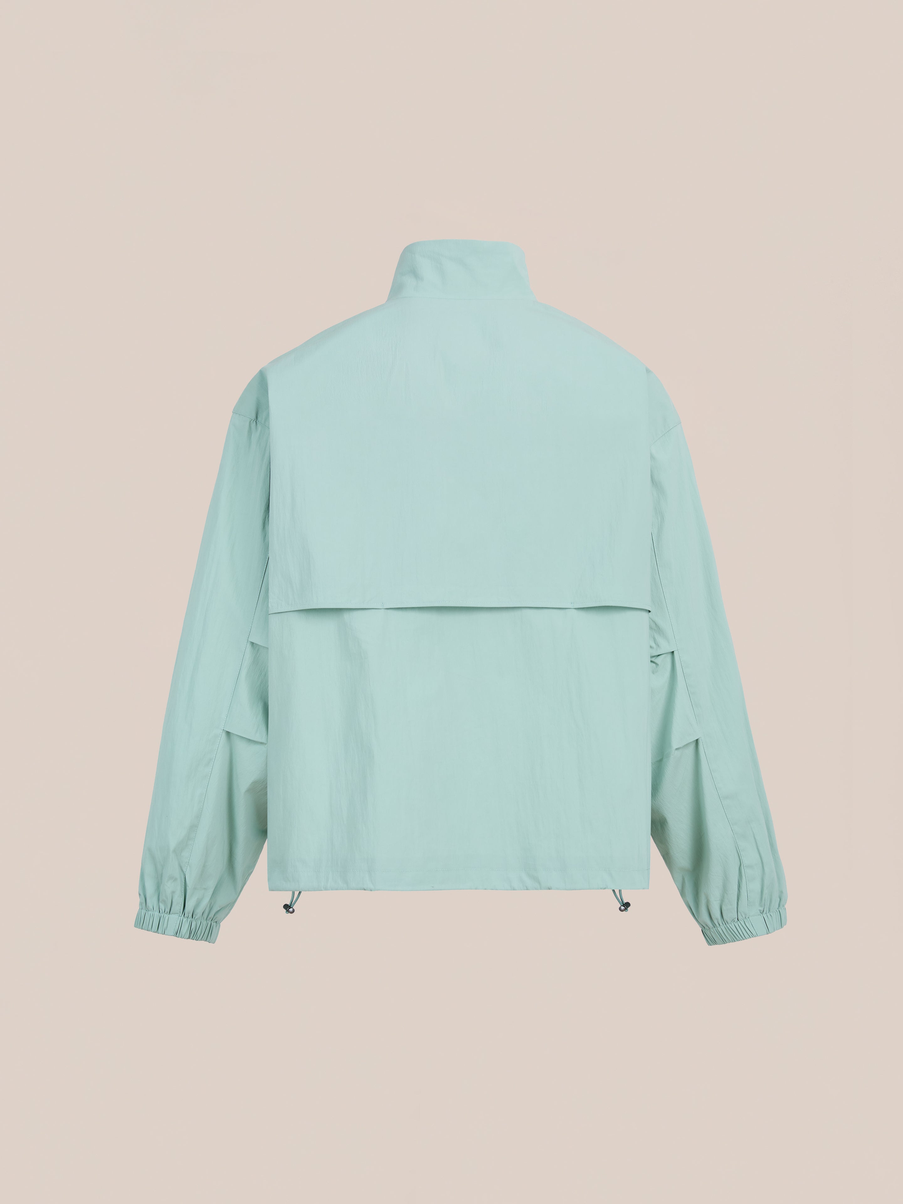 The FOUND Nylon Pocket Track Jacket in light blue features long sleeves, a high collar, elastic cuffs, and a back yoke vent, shown on a plain beige background.