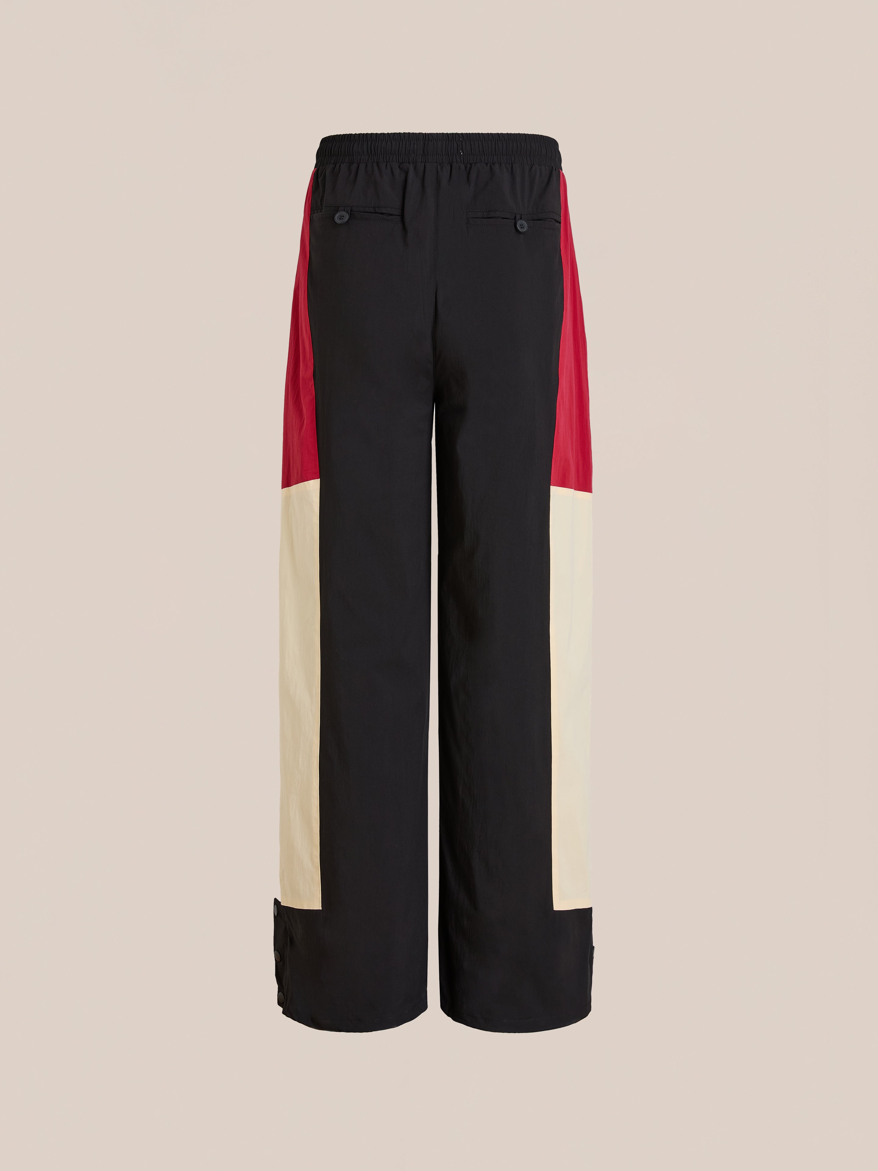 The Pine and Rose Track Pants by Found feature black, beige, and red color blocks, an elastic waistband, and back pockets. These unisex wide-leg pants have a relaxed fit and are shown against a plain background.