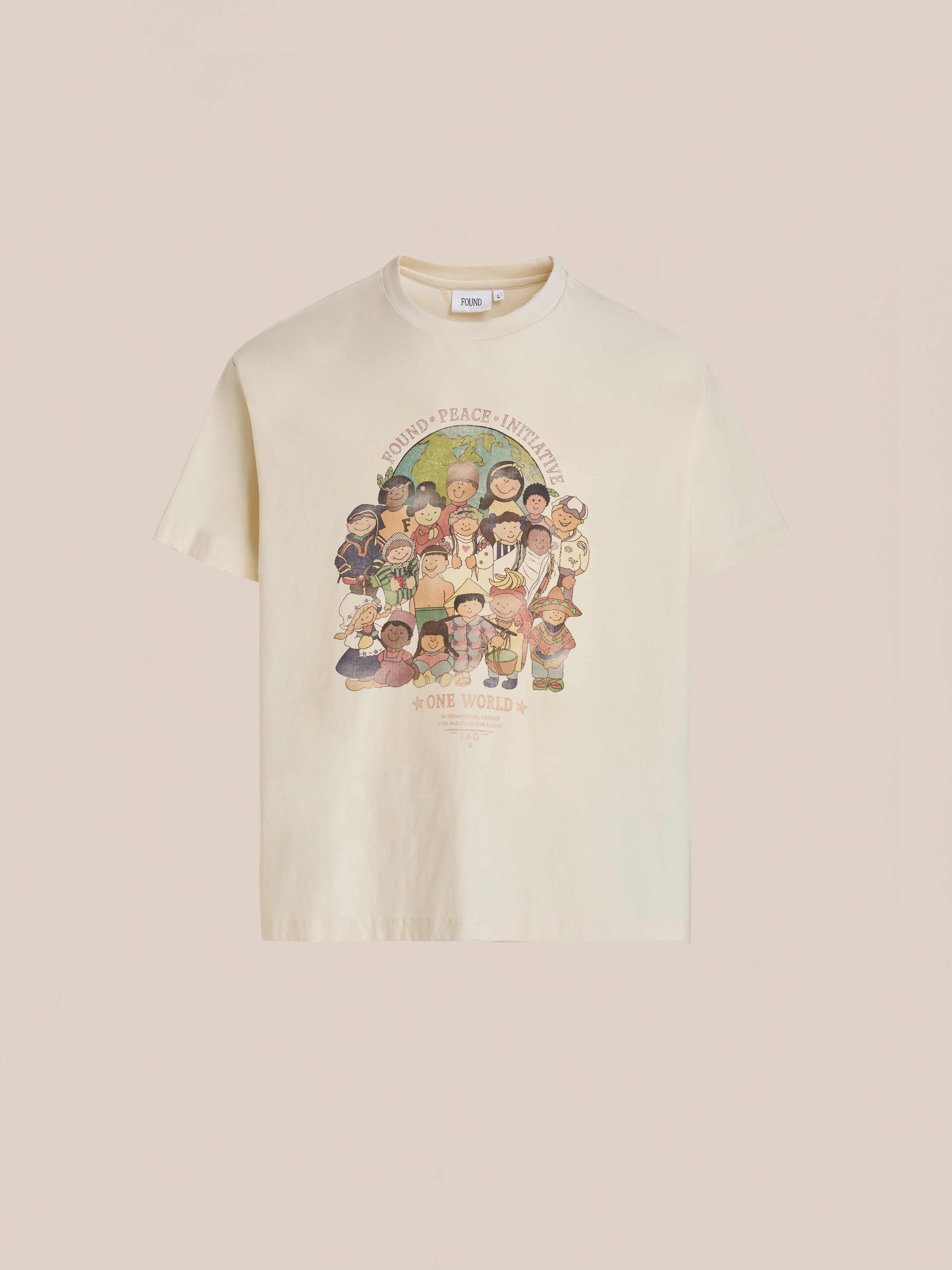 The One World Family Tee by FOUND is a cream-colored shirt featuring diverse children holding hands and “World Peace Initiative” and “One World” printed above and below.