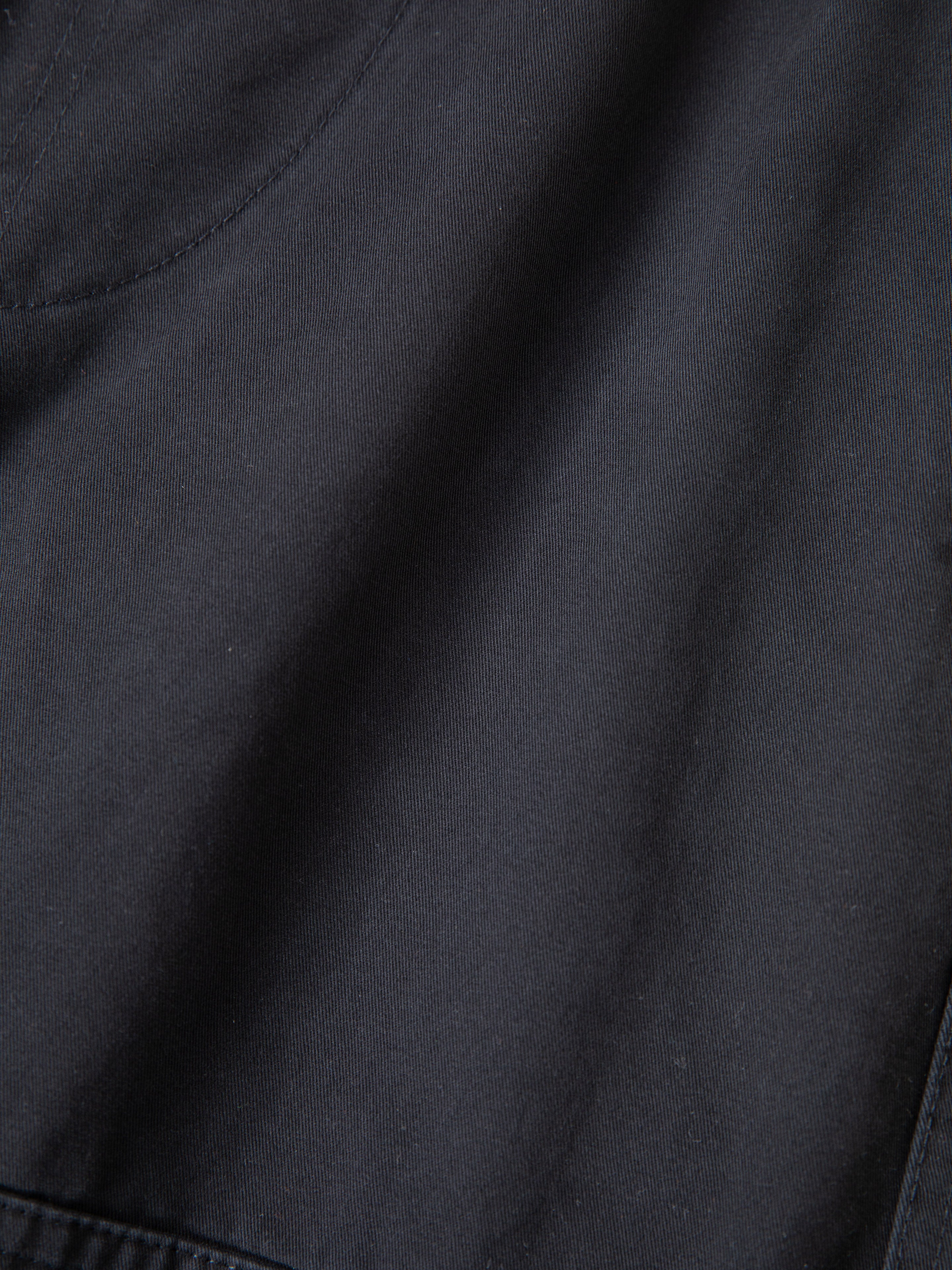 Close-up view of black fabric with visible stitching and a curved seam near the upper left corner, highlighting the durable construction typical of Found's Parachute Cargo Twill Shorts.