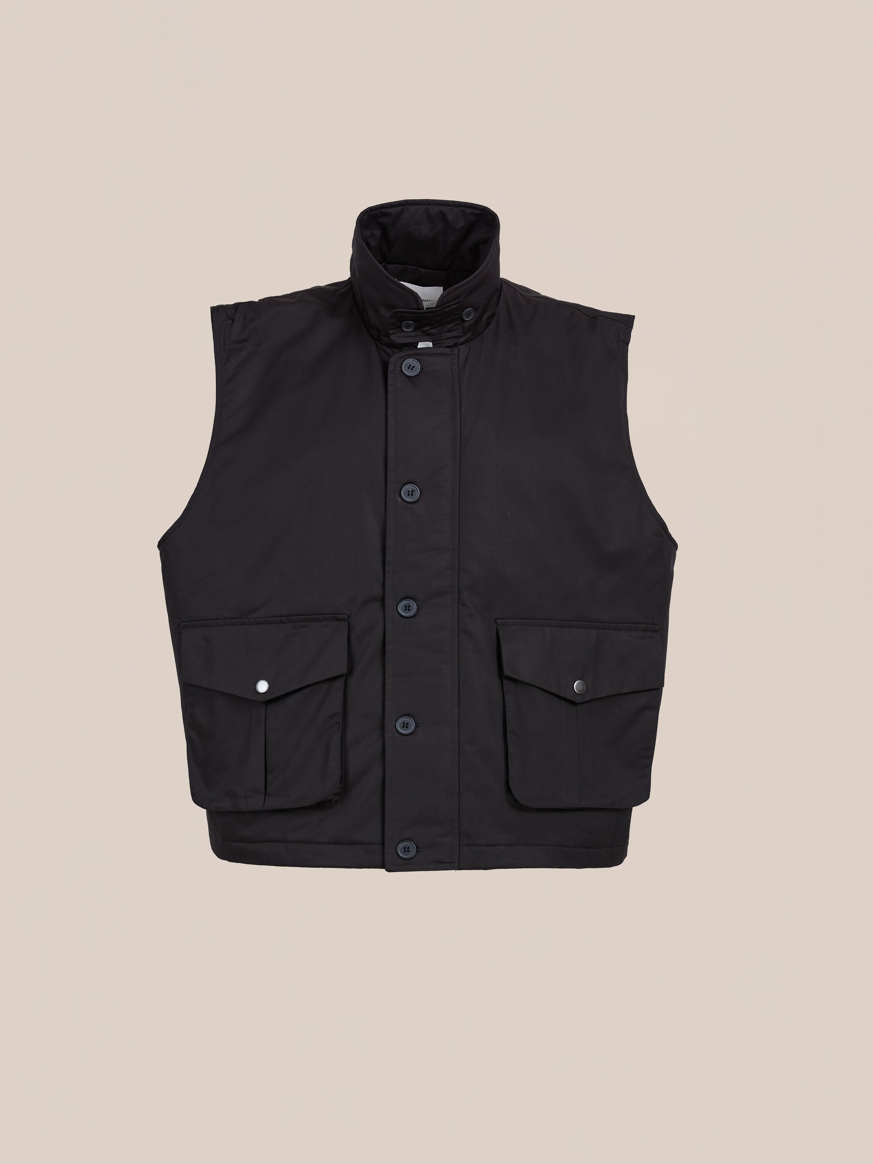 The FOUND Padded Cargo Vest is a black twill utility layer with a high collar, front buttons, and two flap pockets, shown on a beige background—perfect for versatile styling.