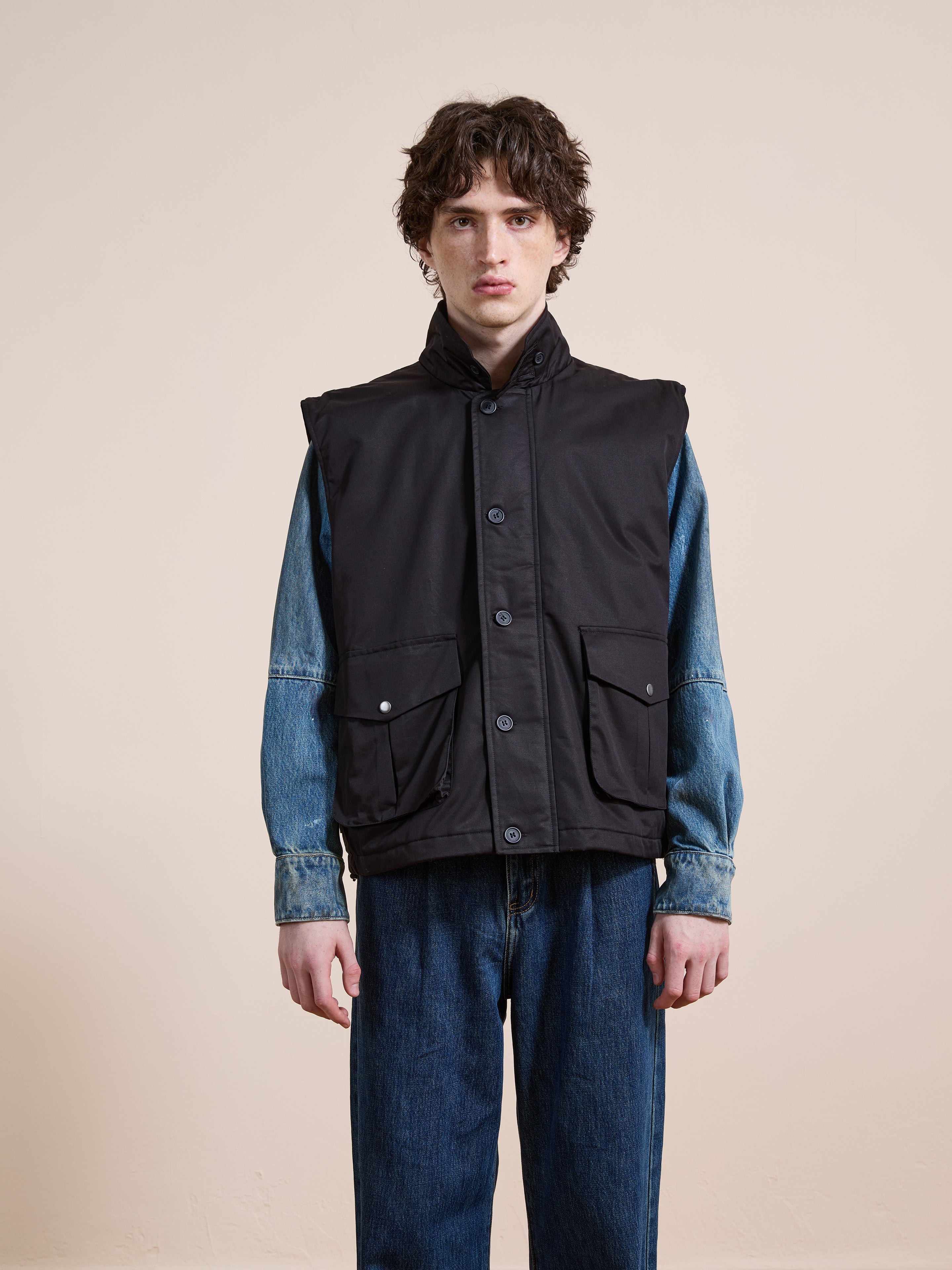 A person stands against a plain background wearing the FOUND Padded Cargo Vest over a denim jacket and blue jeans.