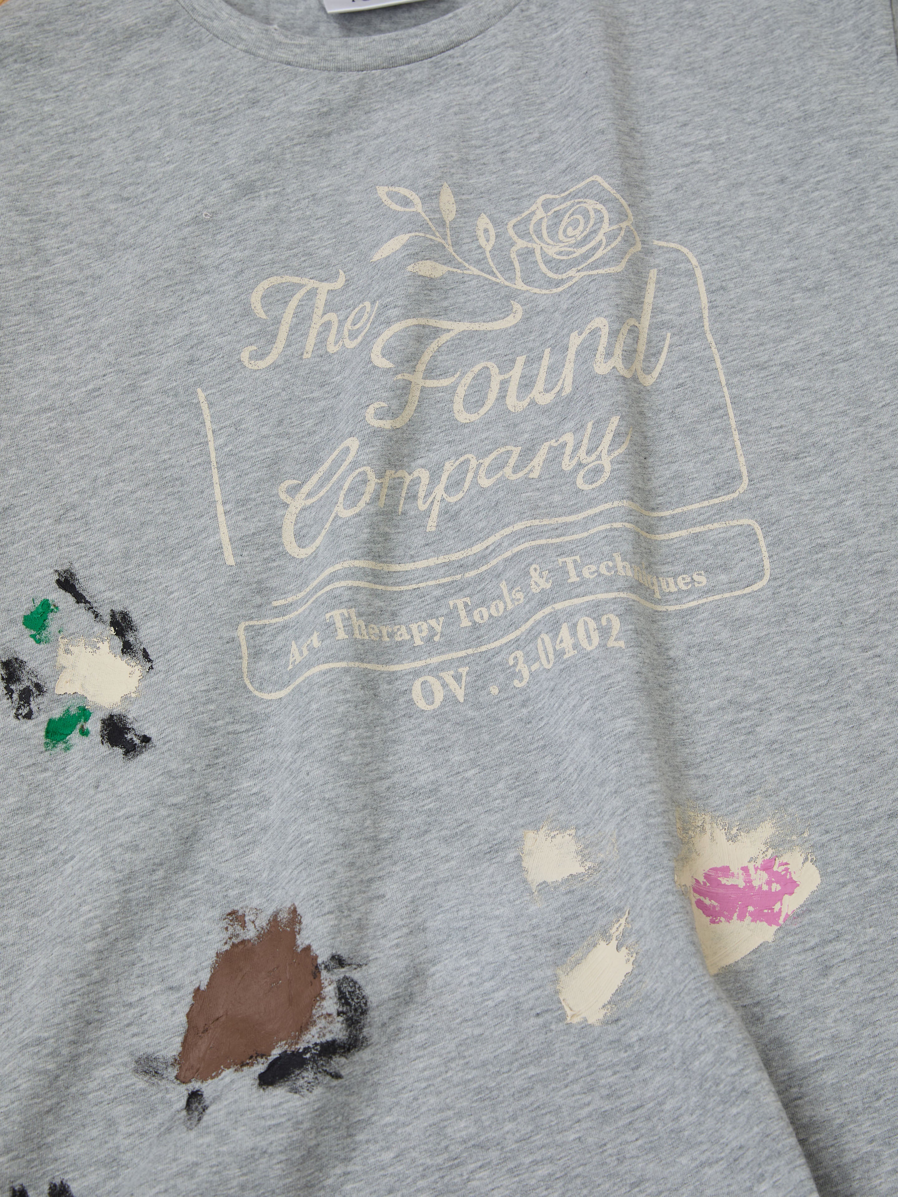 A gray unisex "Painters Company Tee" by FOUND showcases "Art Therapy Tools & Techniques," complemented by vintage-colored paint splatters on the lower part.