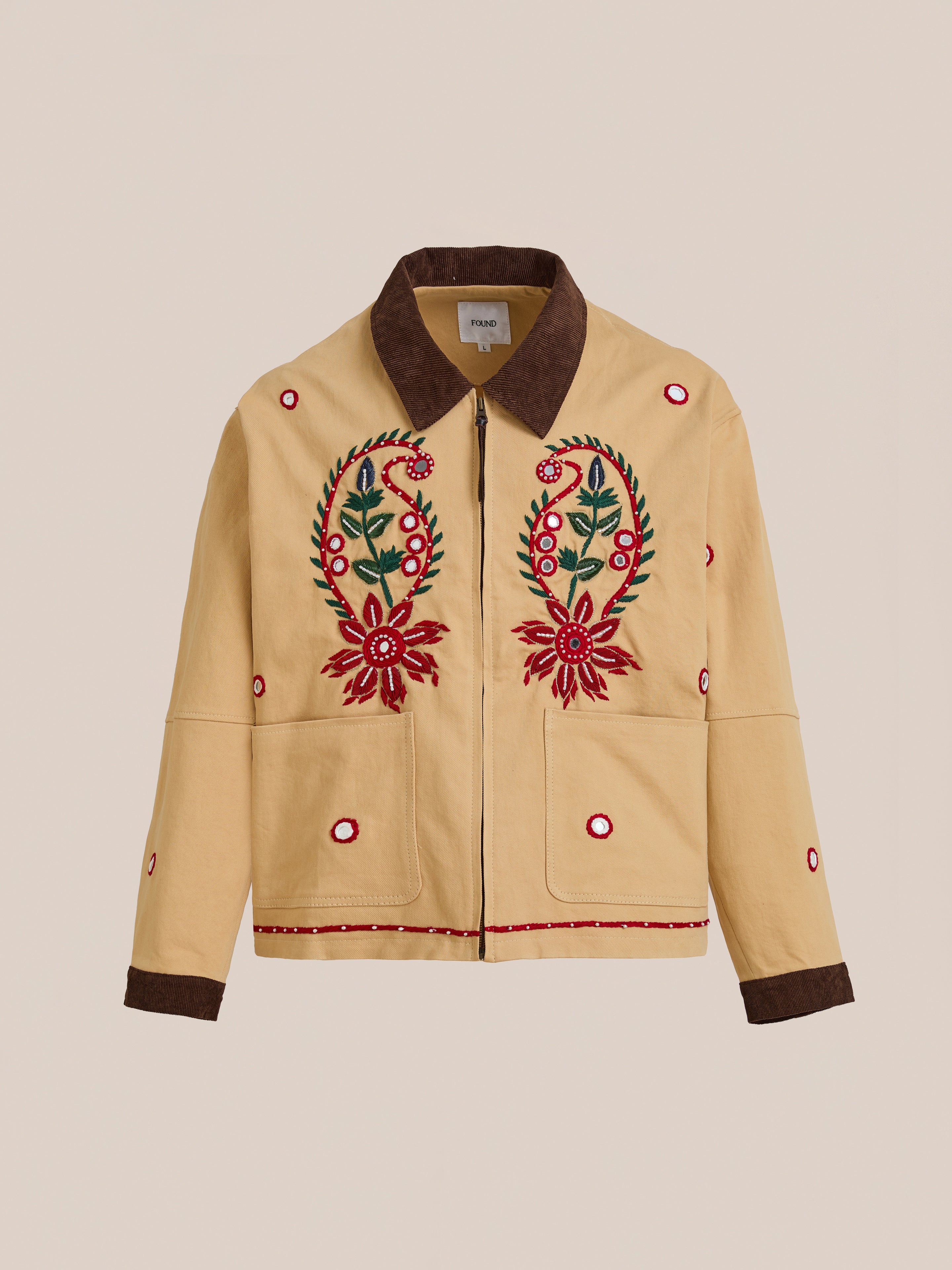 The Found Paisley Motif Hand Embroidered Work Jacket is tan with a dark brown collar and cuffs, red and green paisley floral embroidery, circular red accents, and two pockets, showcasing artisan craftsmanship.