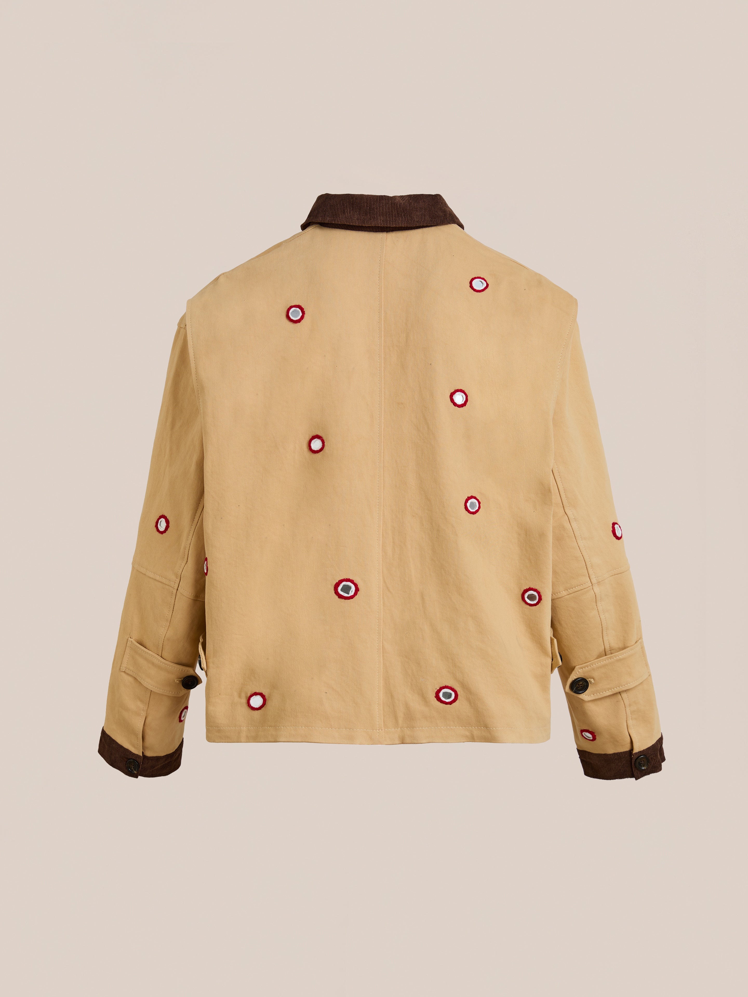 The Found Paisley Motif Hand Embroidered Work Jacket features beige fabric with a dark brown collar and cuffs, accented by red and white circular patches on the back and sleeves. Each piece showcases unique artisan craftsmanship.