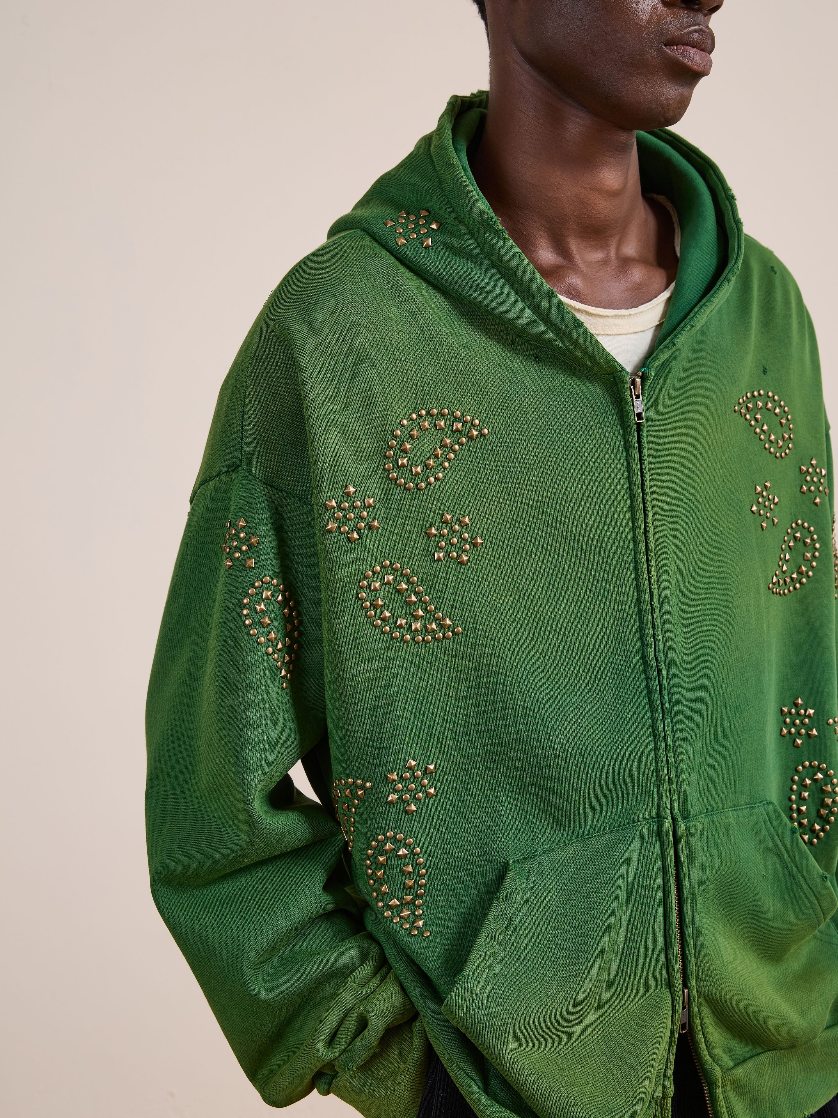A person wears the FOUND Paisley Studded Zip Up Hoodie in green with star stud patterns over a white shirt, shown from the shoulders down—a vintage-inspired unisex style.