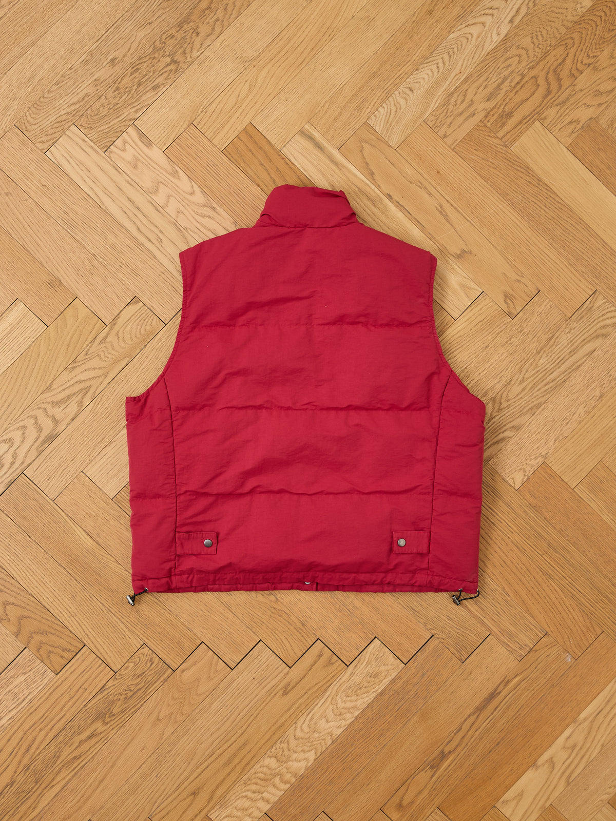 FOUND Patch Down Vest laid flat, back side up, on a light wooden herringbone floor.