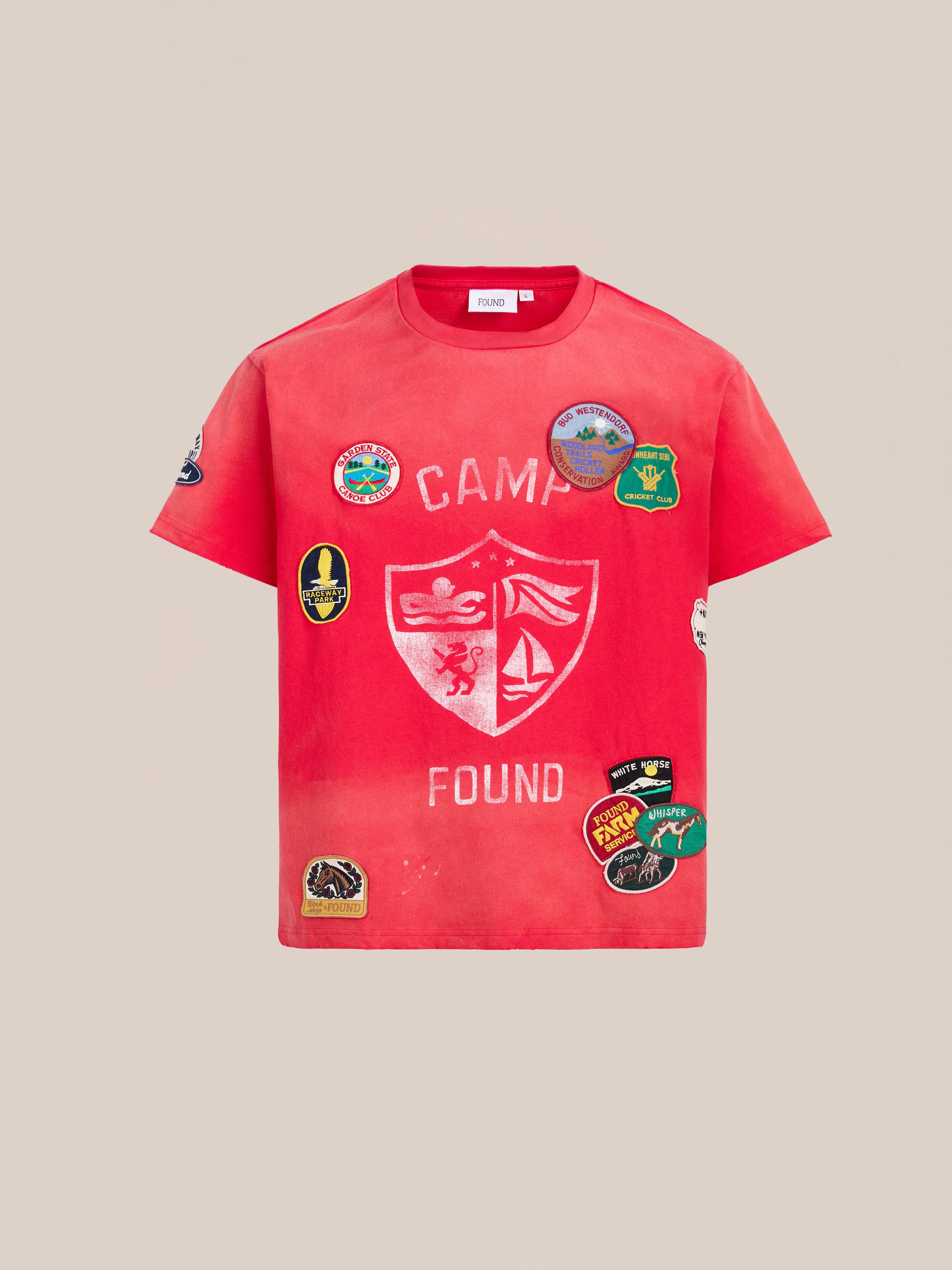 The FOUND Patchwork Camp Tee is a red unisex cotton t-shirt featuring "CAMP FOUND" text, shield graphic, and colorful embroidered patches on the front and sleeves for a bold, playful look.