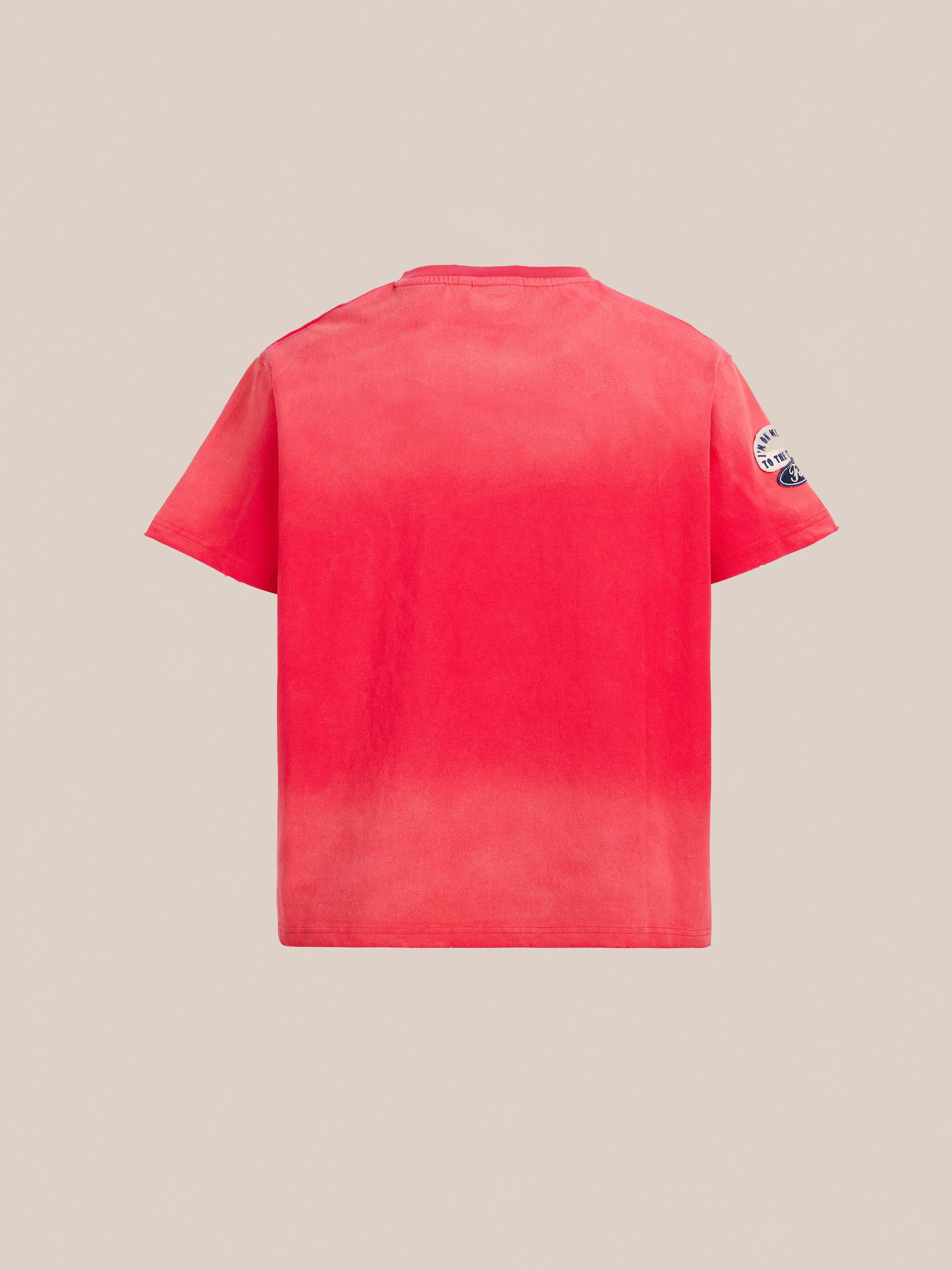 The FOUND Patchwork Camp Tee is a plain red unisex cotton shirt shown from the back, featuring a round neckline and a small white patch on the left sleeve for a classic look.