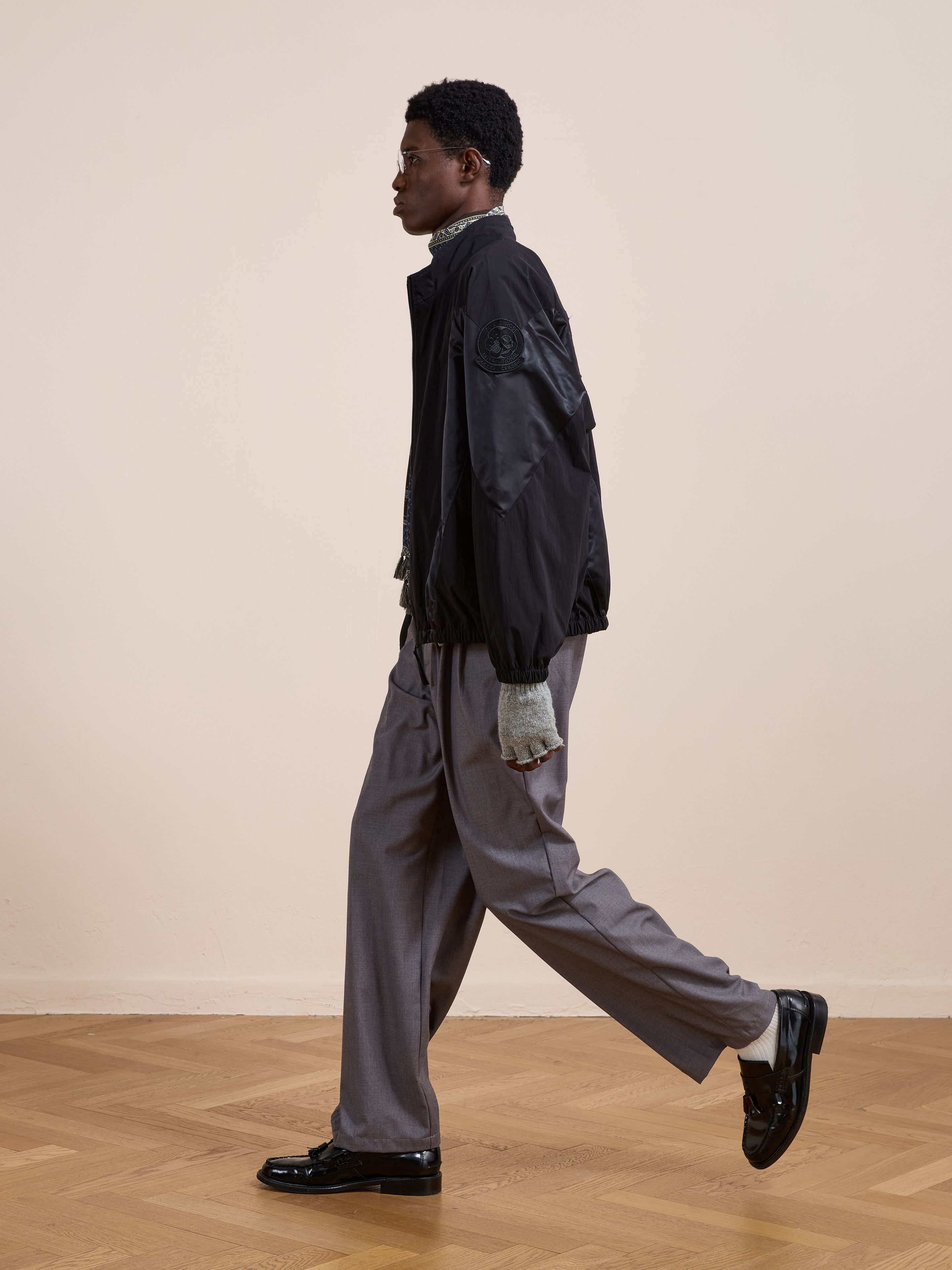 A man wearing the FOUND Pine and Rose Jacket walks indoors on a wooden floor against a plain beige wall.