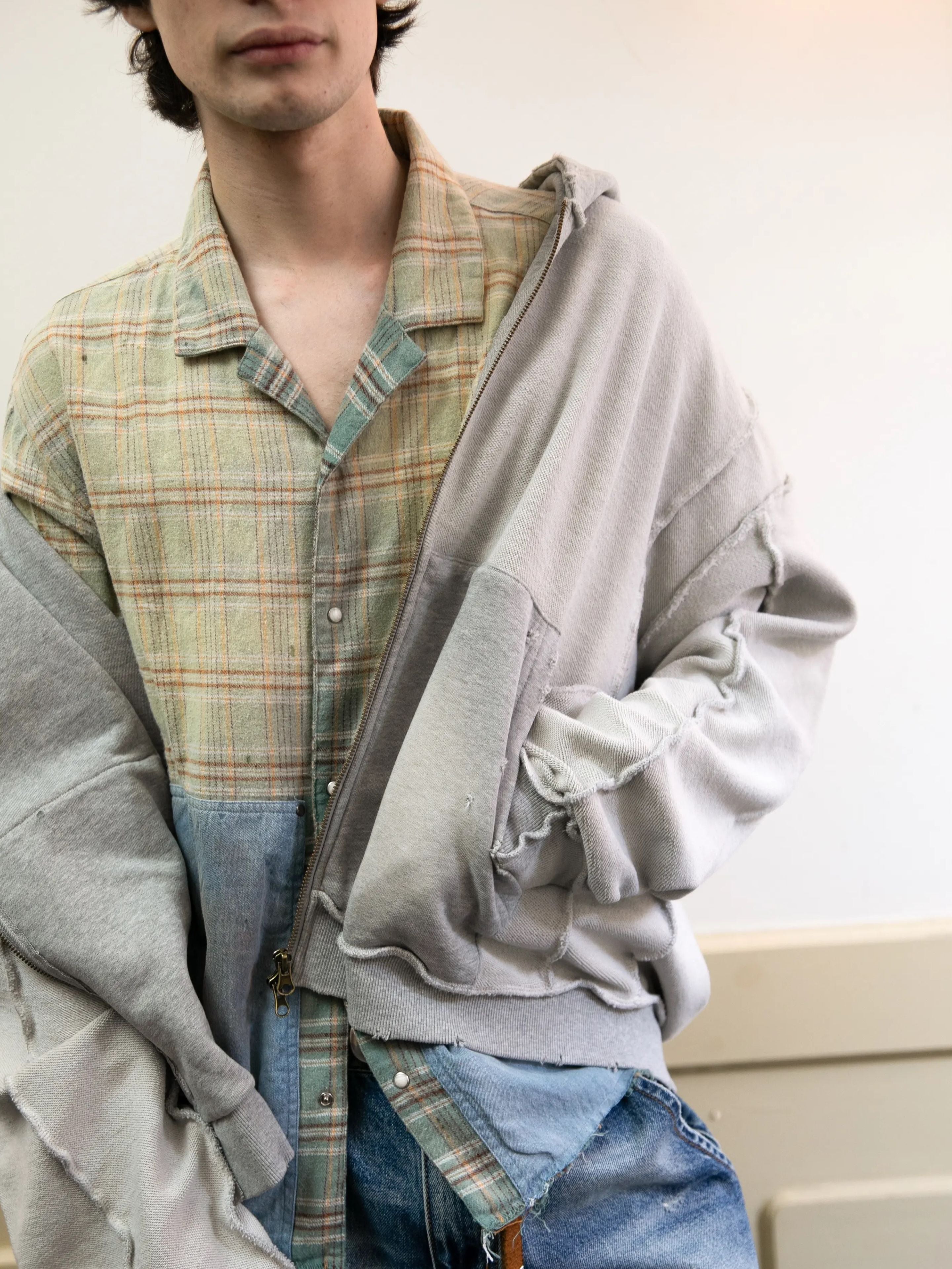 Model wears the FOUND Plaid Denim Shirt—unisex, relaxed fit—styled under a light gray oversized zip-up hoodie with blue jeans, standing against a simple indoor backdrop.