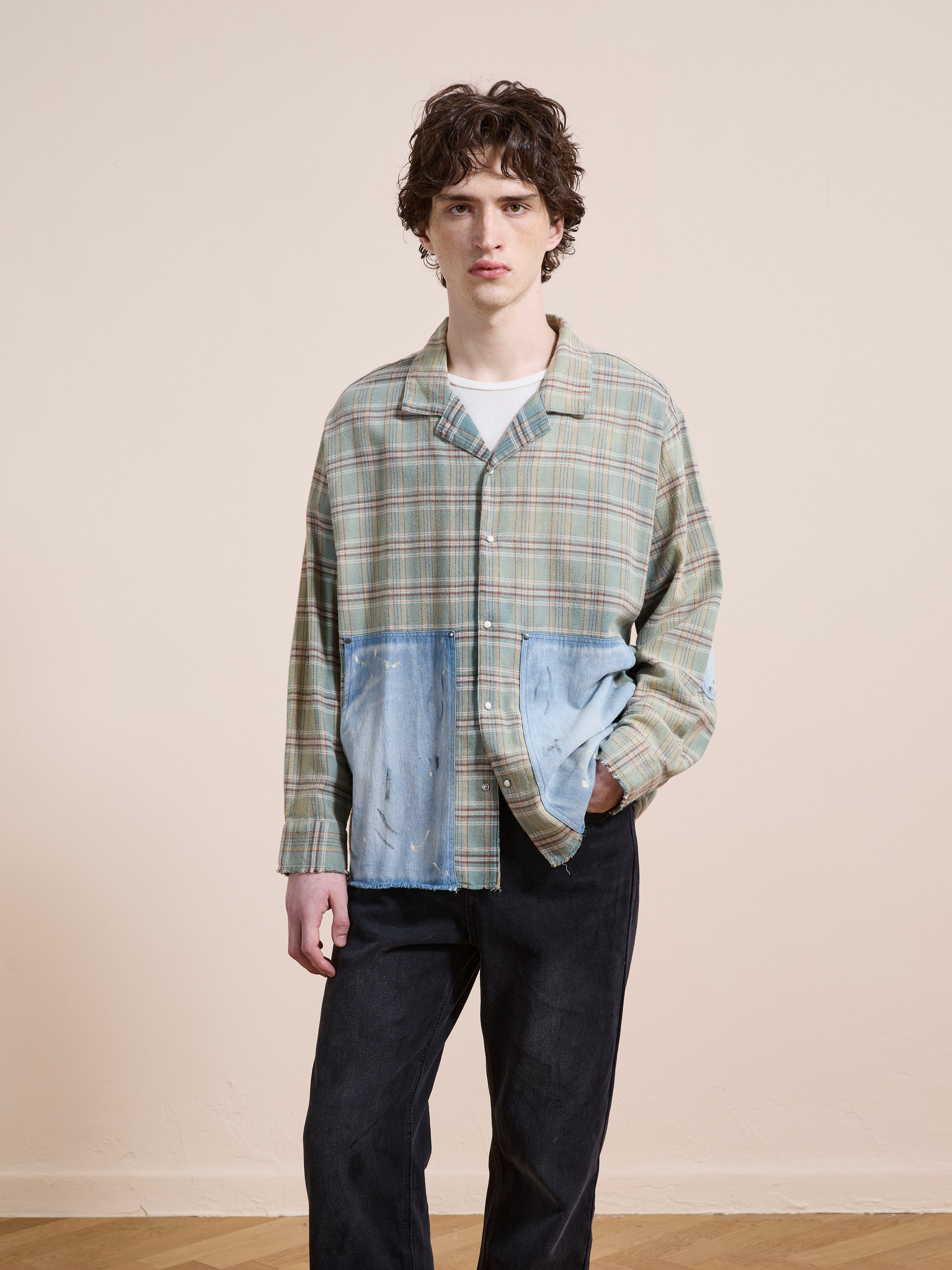 A person stands indoors wearing the FOUND Plaid Denim Shirt over a white tee with black pants, one hand in their pocket—showcasing effortless unisex workwear style.