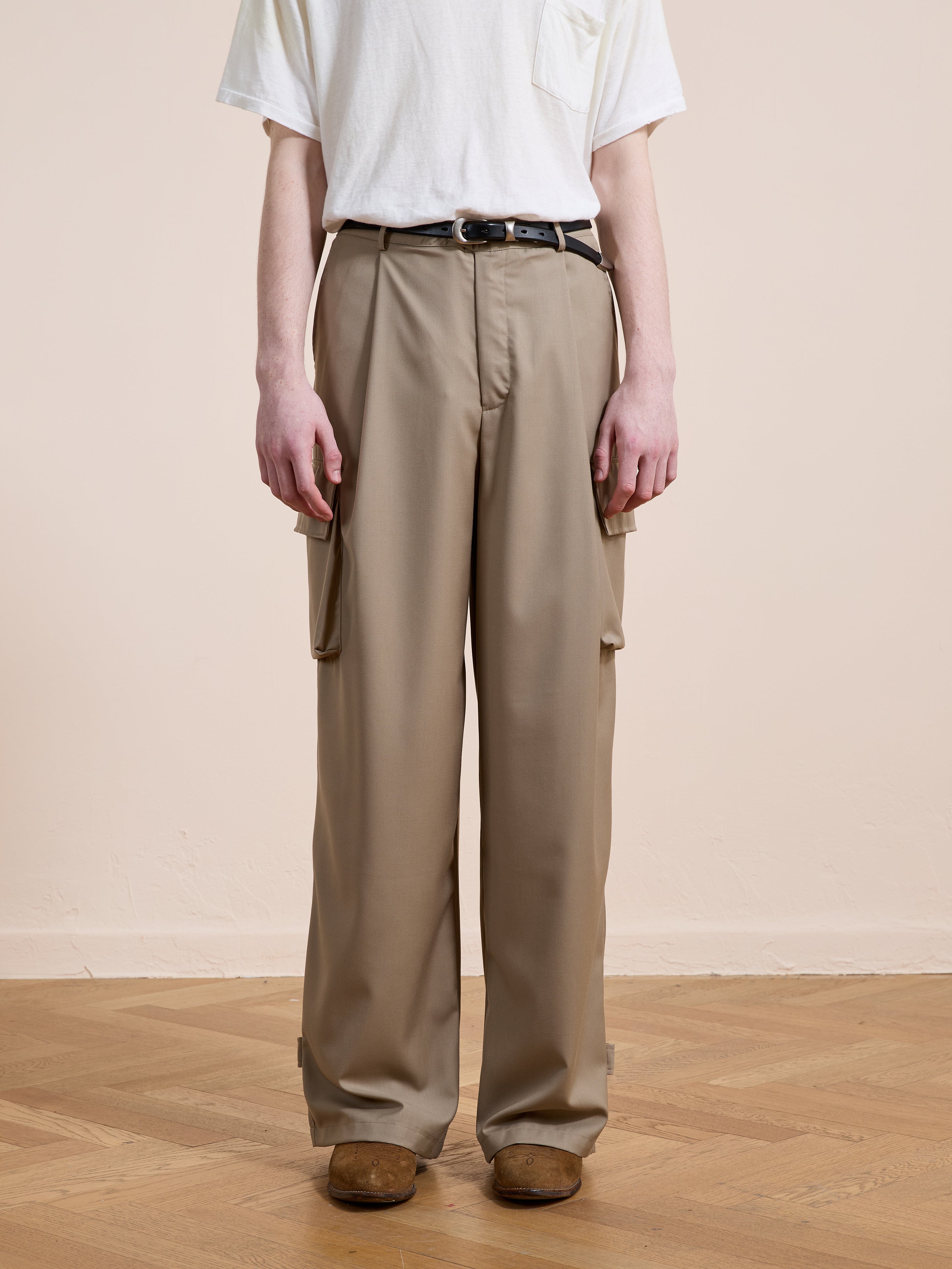 Person wearing FOUND Pleated Cargo Pants, a white t-shirt, black belt, and brown shoes, standing on a wooden floor against a plain light background.