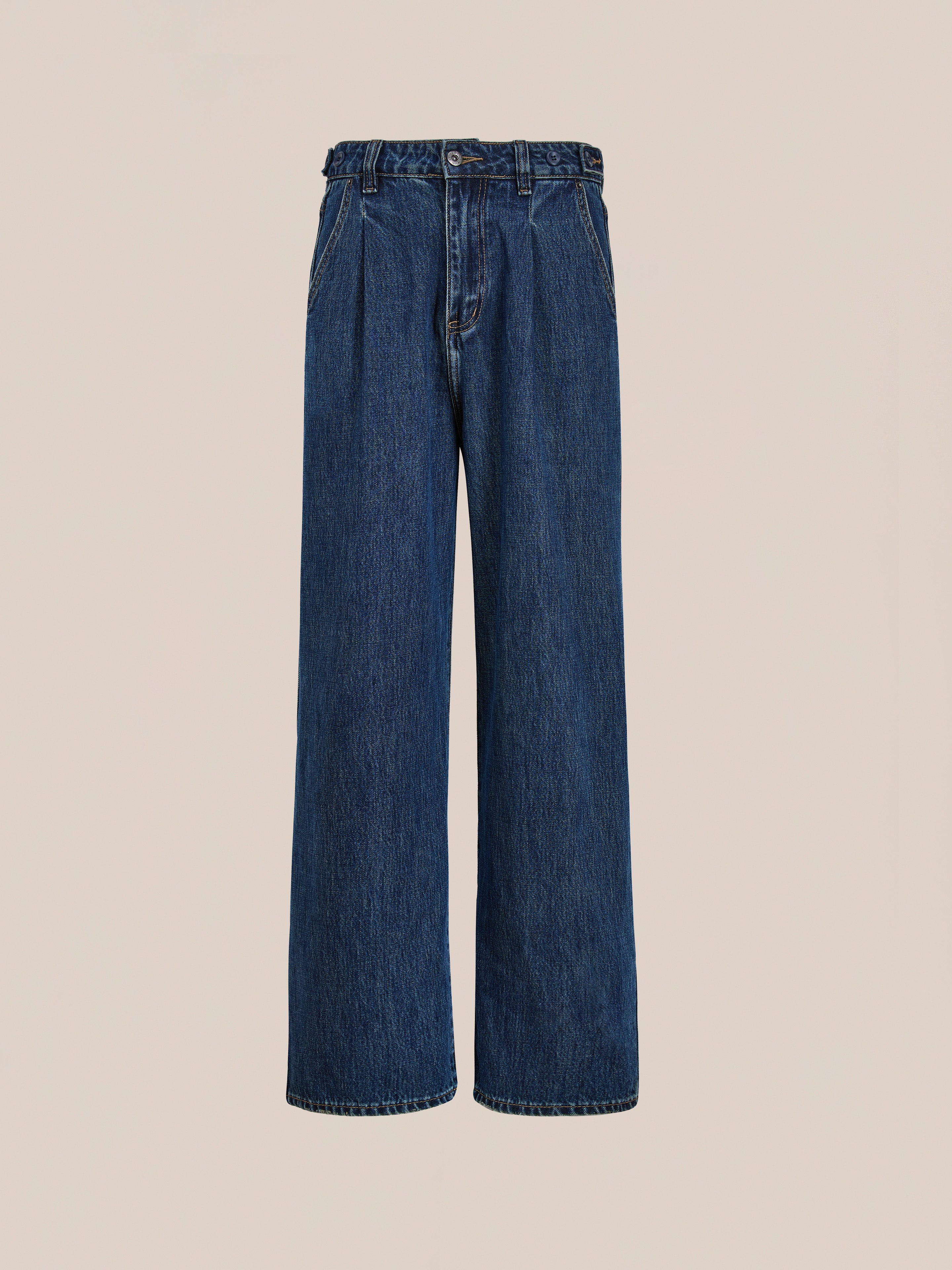 The Found Pleated Relaxed Fit Jeans feature wide-leg blue vintage denim, a high waist, pleated front, button closure, and front pockets. This unisex style is shown against a plain beige background.