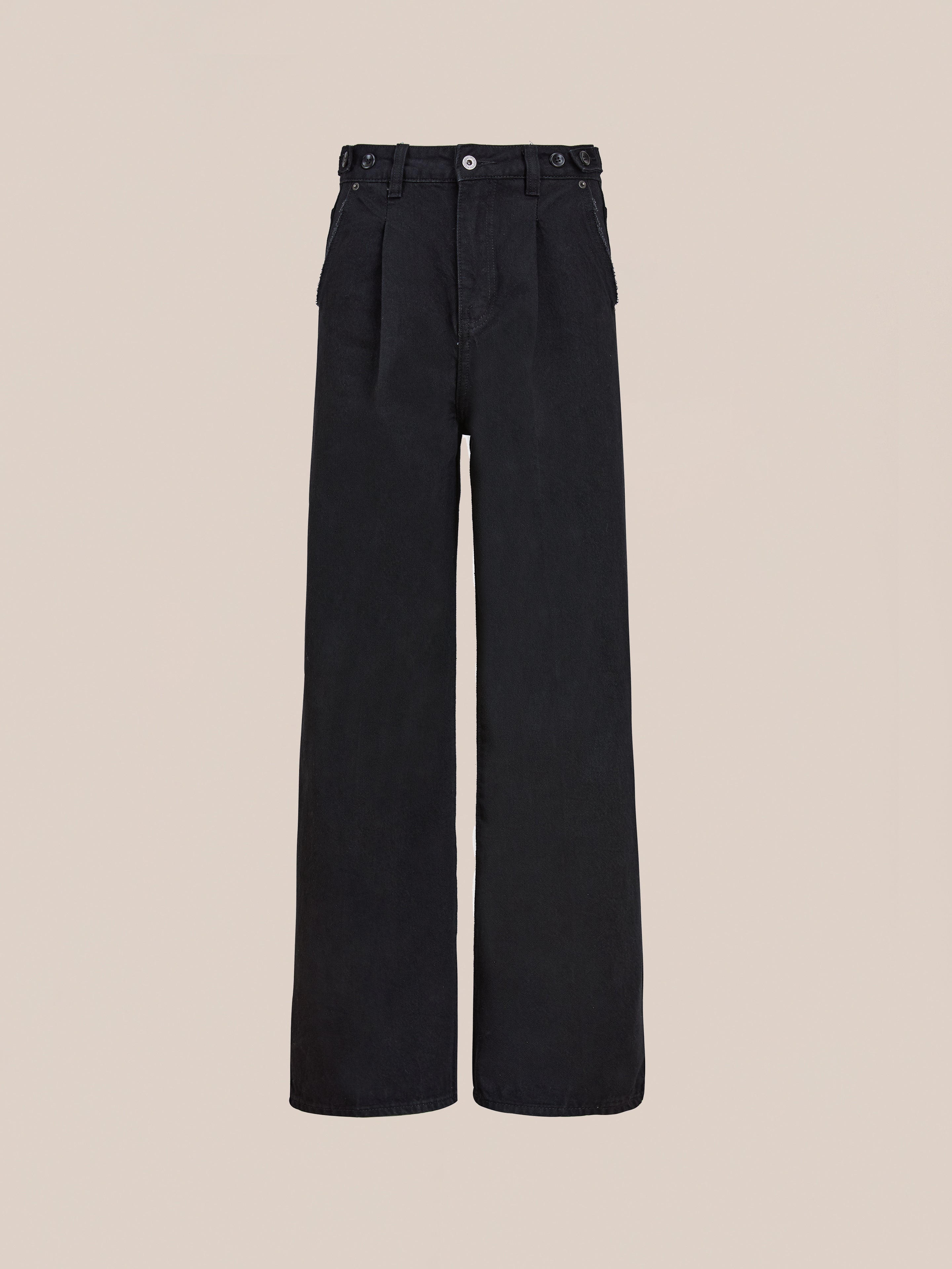 The Found Pleated Relaxed Fit Jeans are high-waisted, wide-leg unisex black jeans featuring button and zip closure, belt loops, and side pockets, shown against a plain beige background.