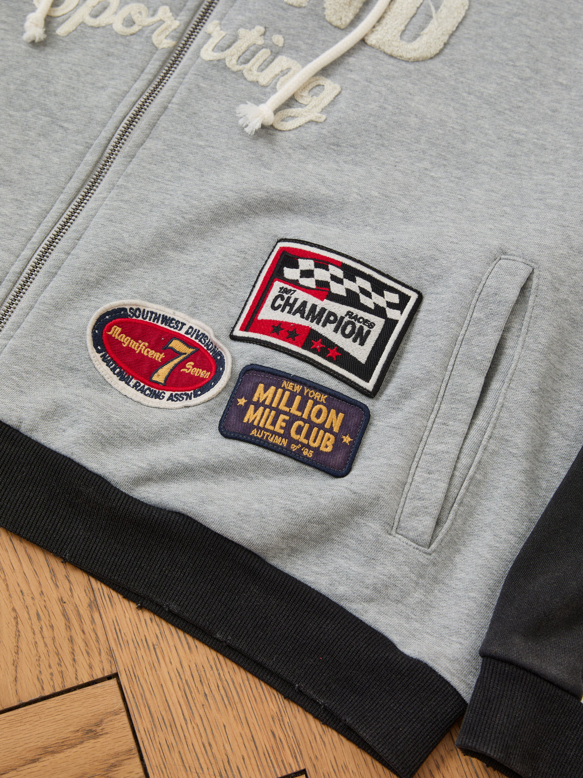 The FOUND Racer Hoodie features three vibrant embroidered patches—“Champion,” “Million Mile Club,” and “Magnificent Seven”—for a classic vintage sportswear vibe.